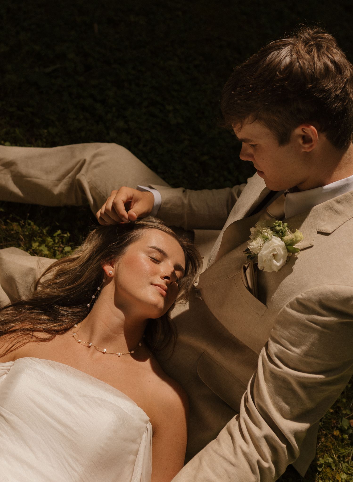 Couple in formal wedding attire laying together in warm sunlight.