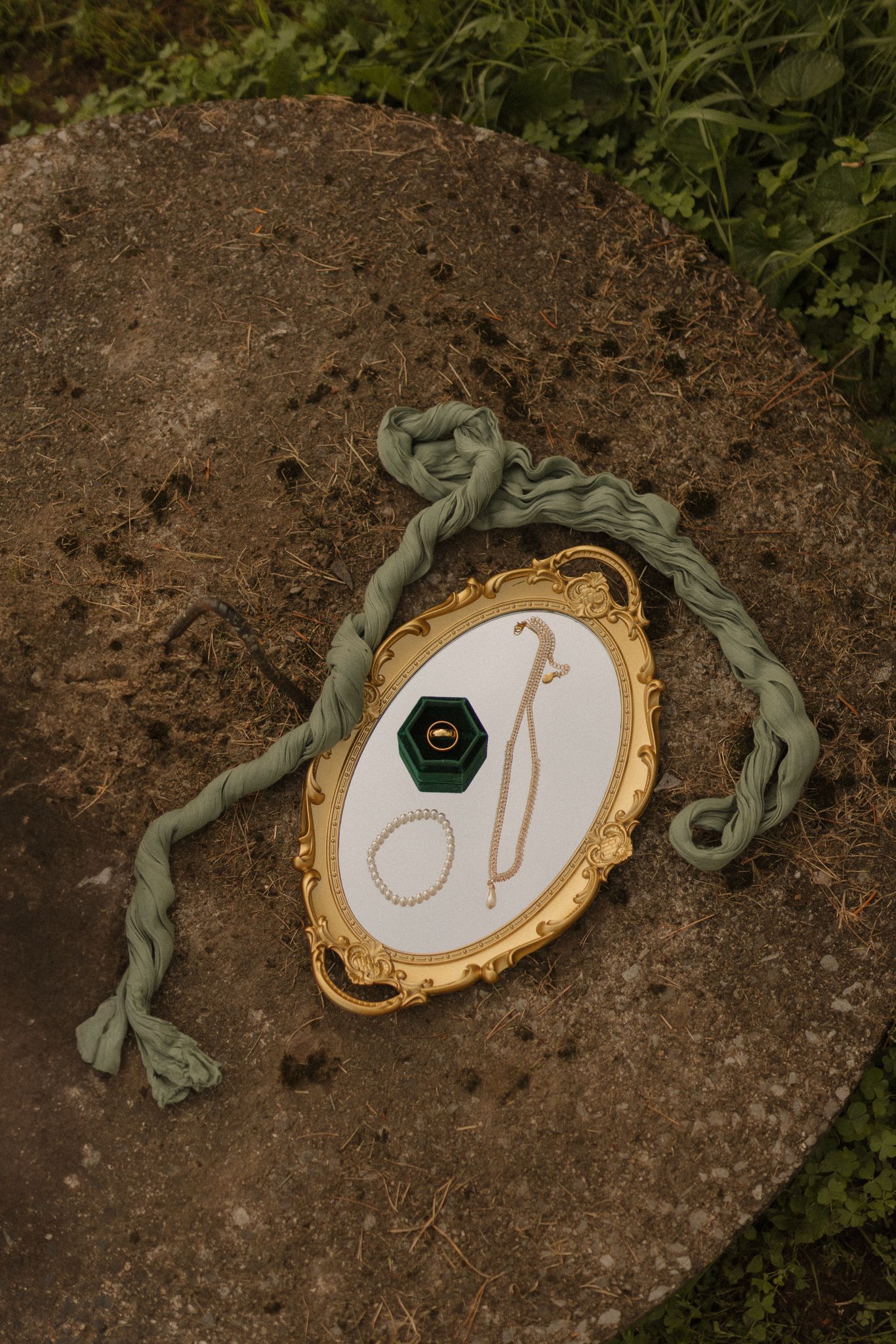 Wedding rings displayed on ornate gold-rimmed trays with sage green ribbon accents.