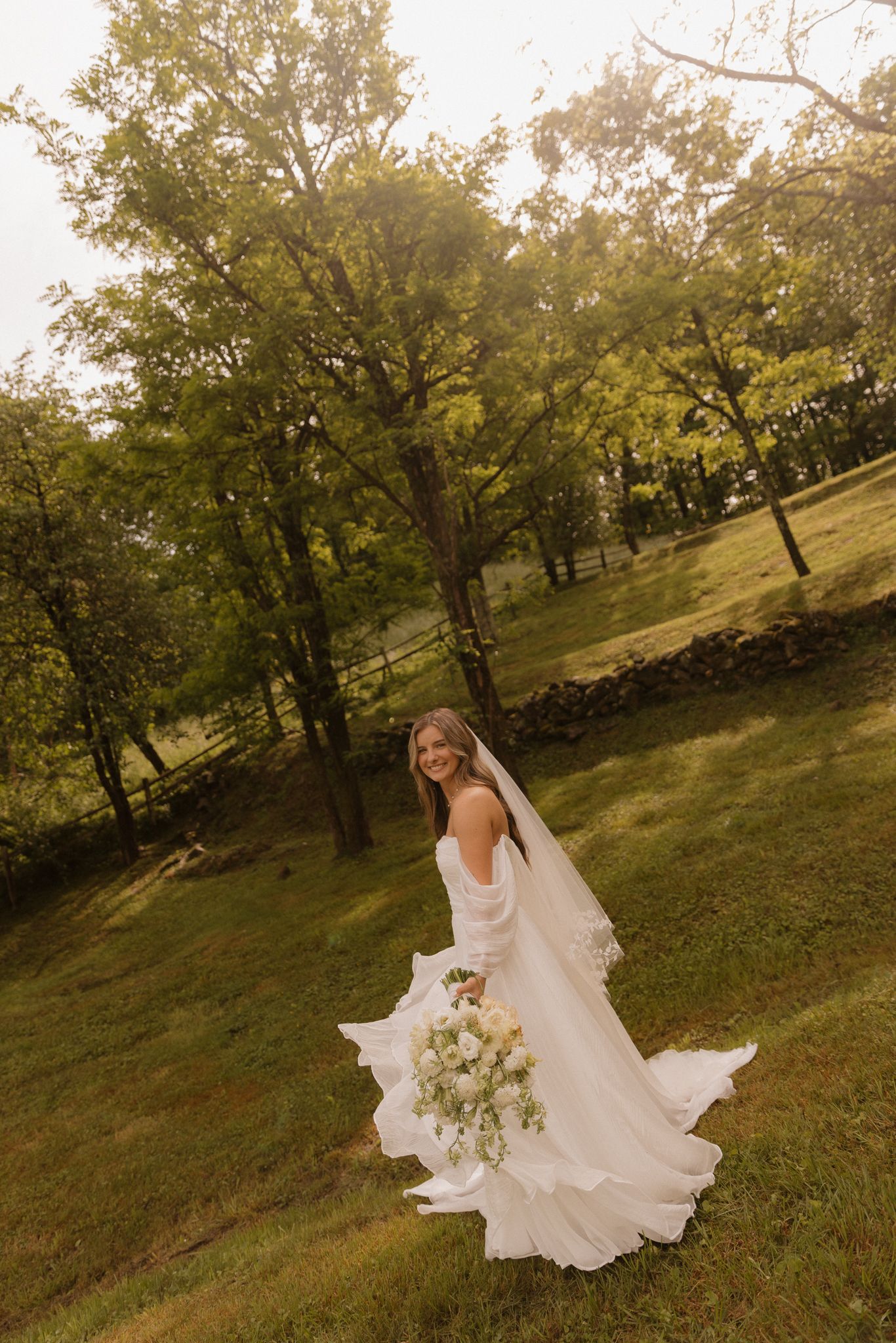 Bride in flowing white dress twirling in a sunlit autumn garden.