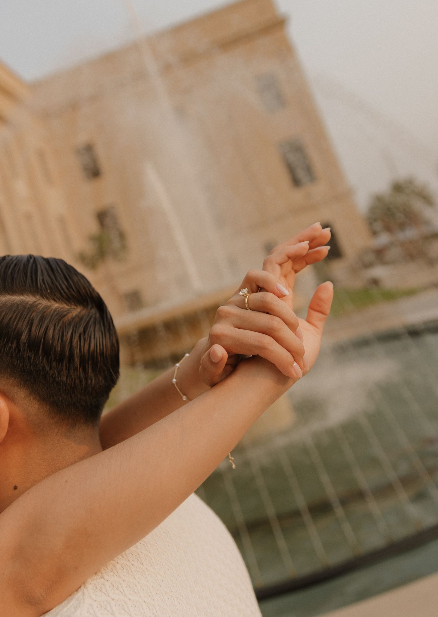 Close-up of clasped hands during wedding dance with fountain in background.
