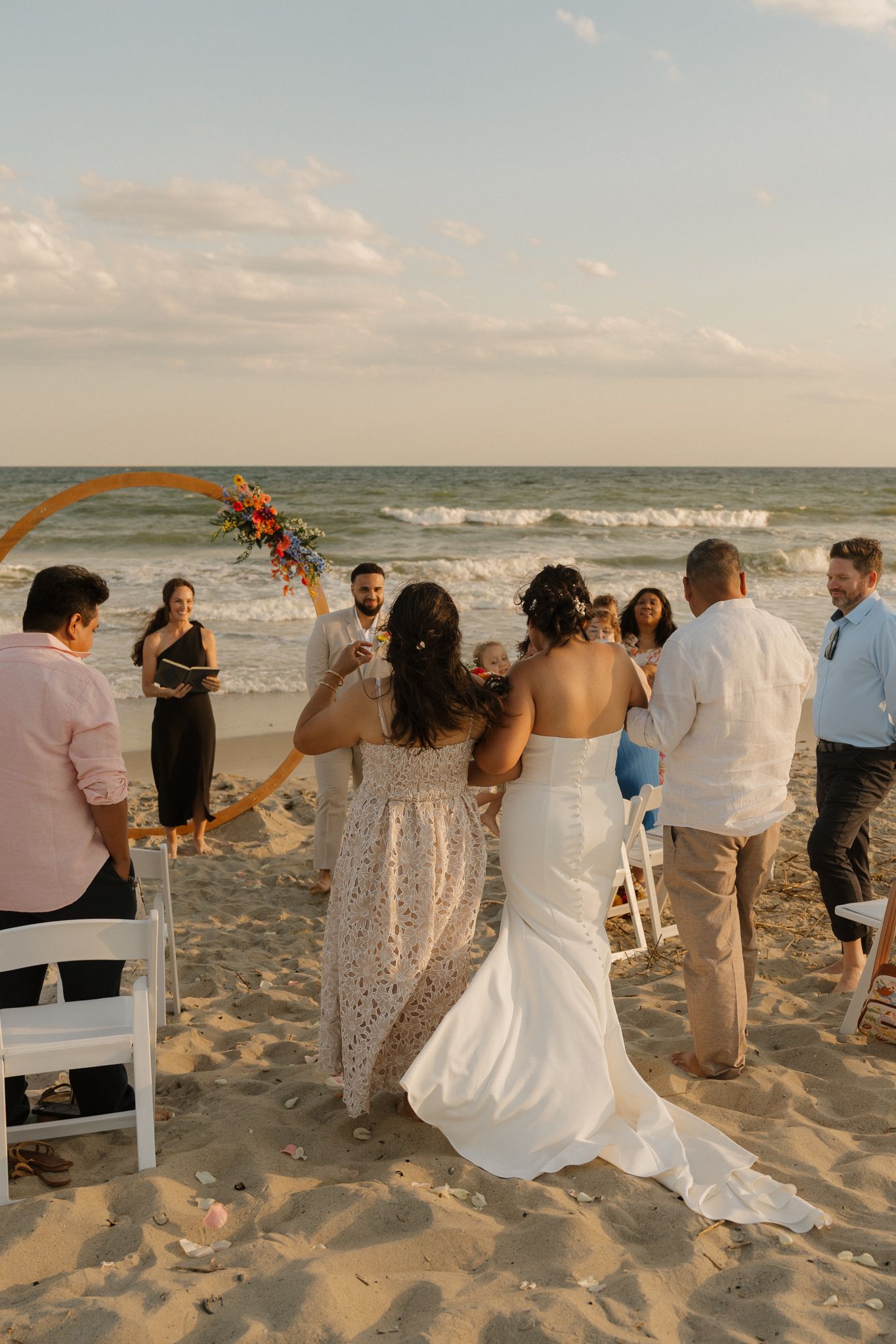 A beach wedding ceremony at sunset with guests gathered around on the sand.