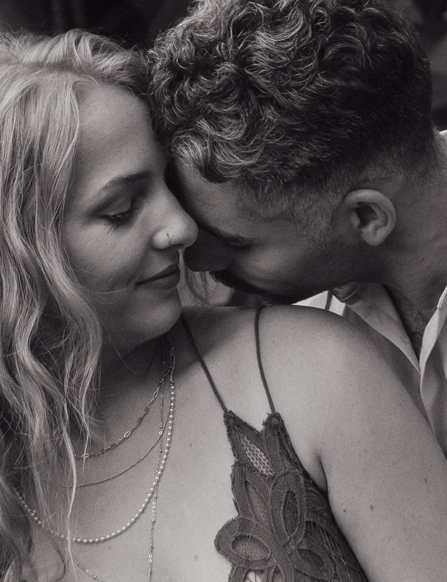 A romantic black and white portrait of a couple in an intimate embrace with elegant jewelry details.