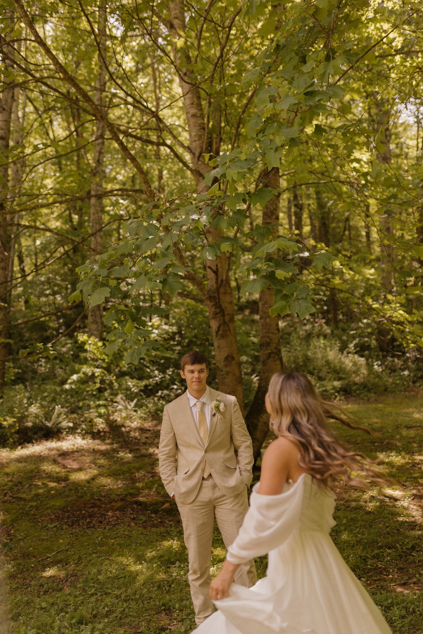 A wedding couple poses in a sunlit forest setting with green leaves and natural lighting.