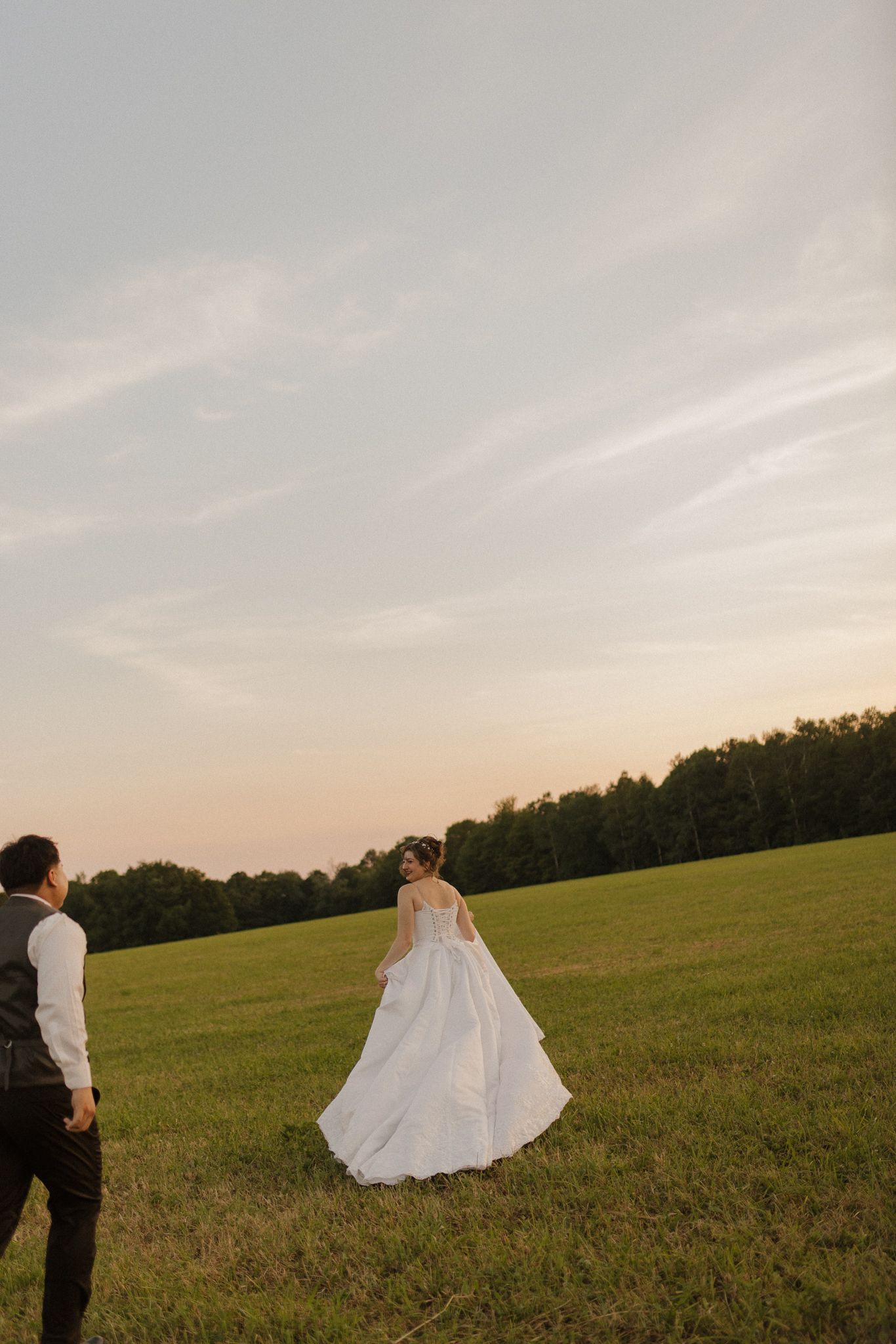A couple walks through a grassy meadow at sunset with the bride's dress flowing in the breeze.