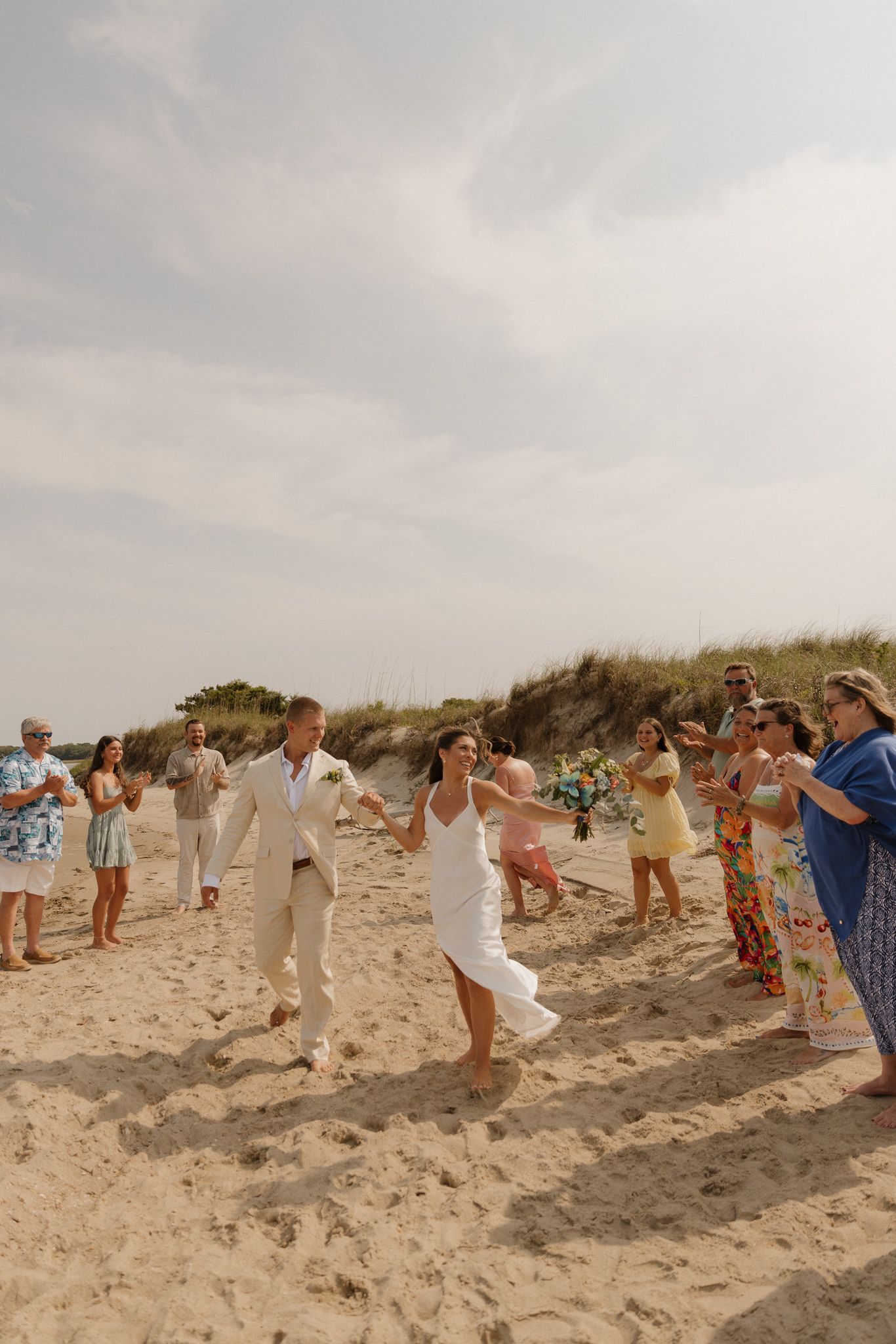 Wedding guests standing on a sandy beach watching a celebratory moment during a seaside ceremony.