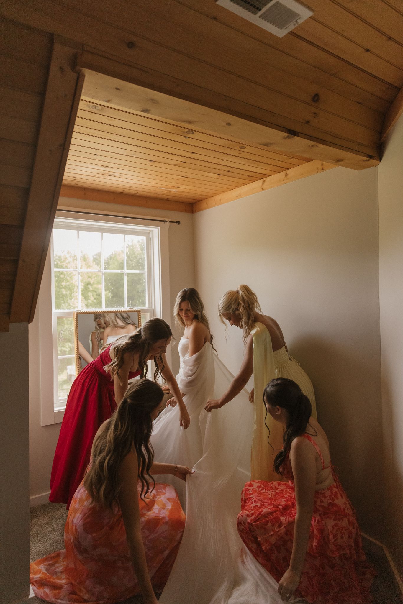 Getting ready scene with bridesmaids helping adjust wedding dress.
