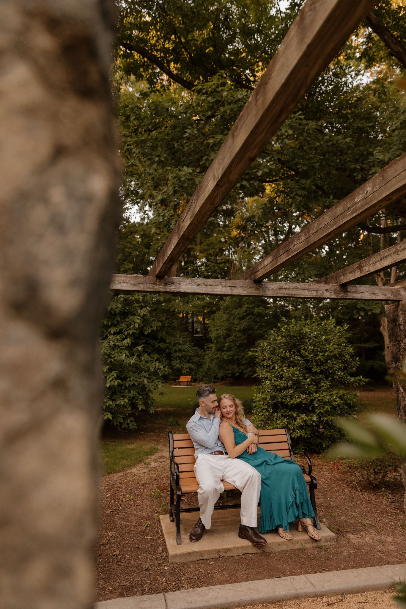 A couple relaxing on a wooden bench under a pergola in a garden setting.