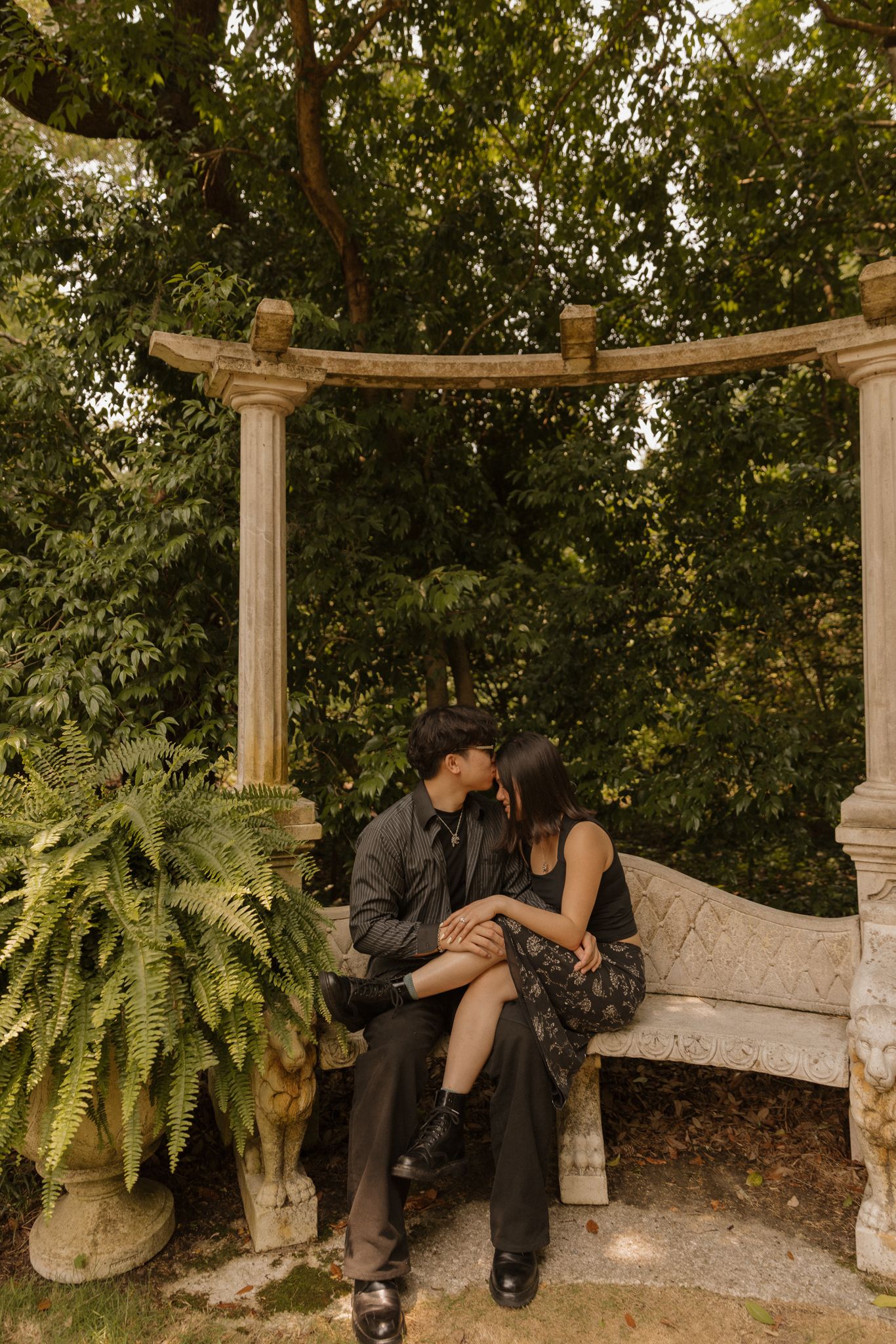Couple sharing an intimate moment on a garden bench under a pergola with hanging ferns.