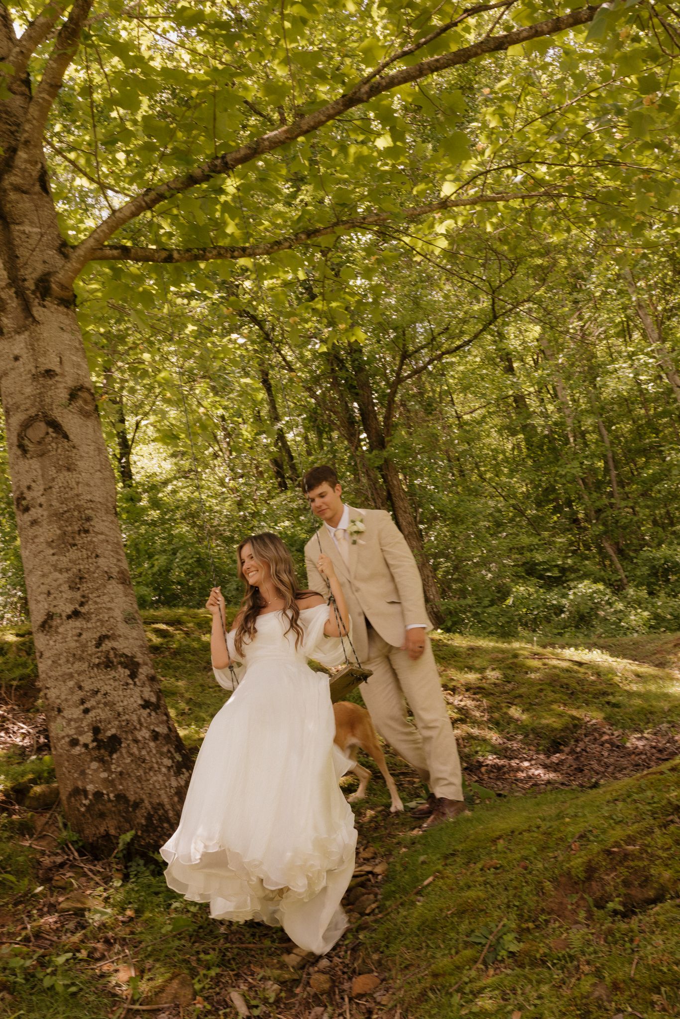 Newlyweds share a playful moment in a sunlit forest setting.