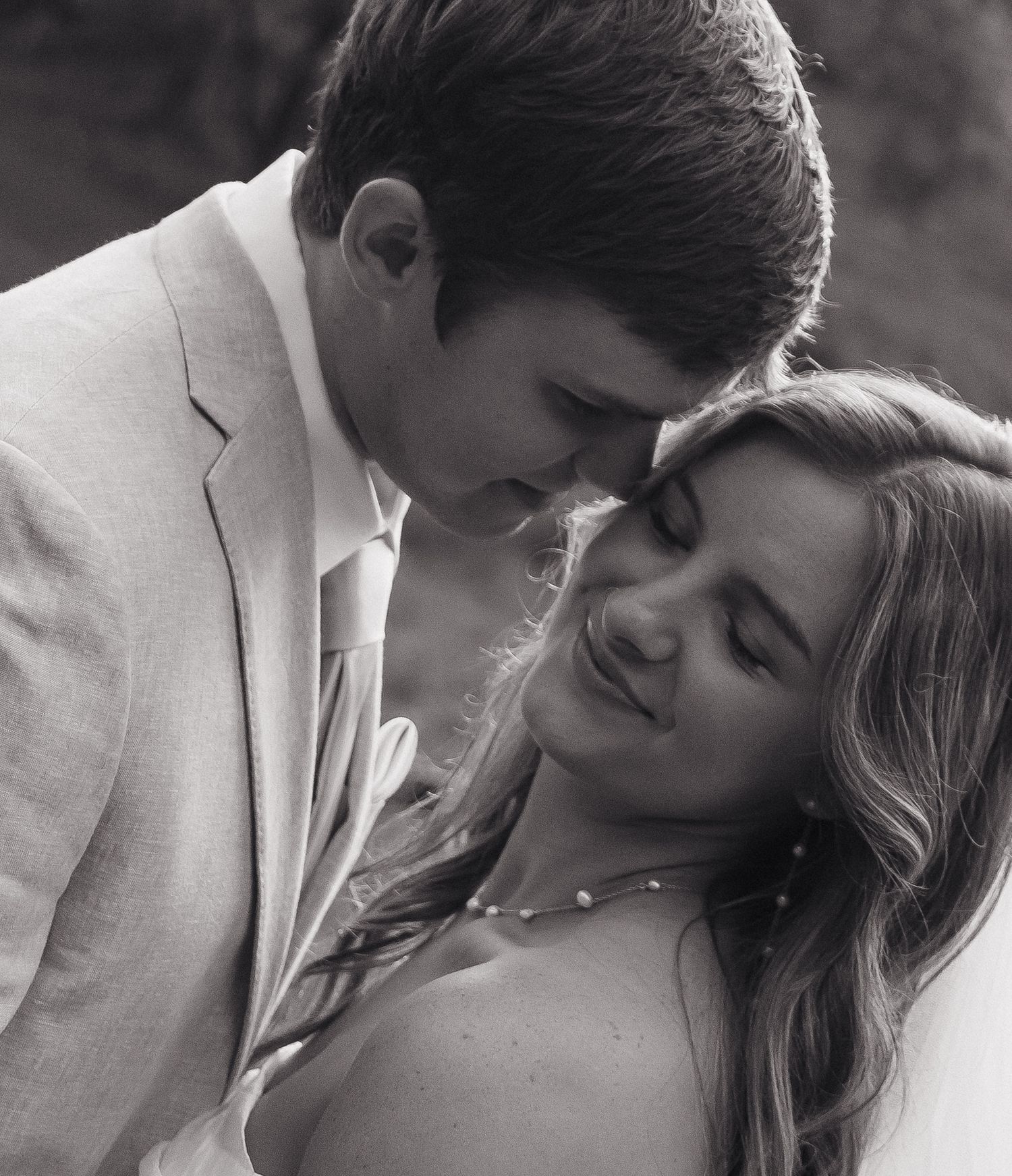 Intimate black and white portrait of newlyweds sharing a tender moment outdoors.