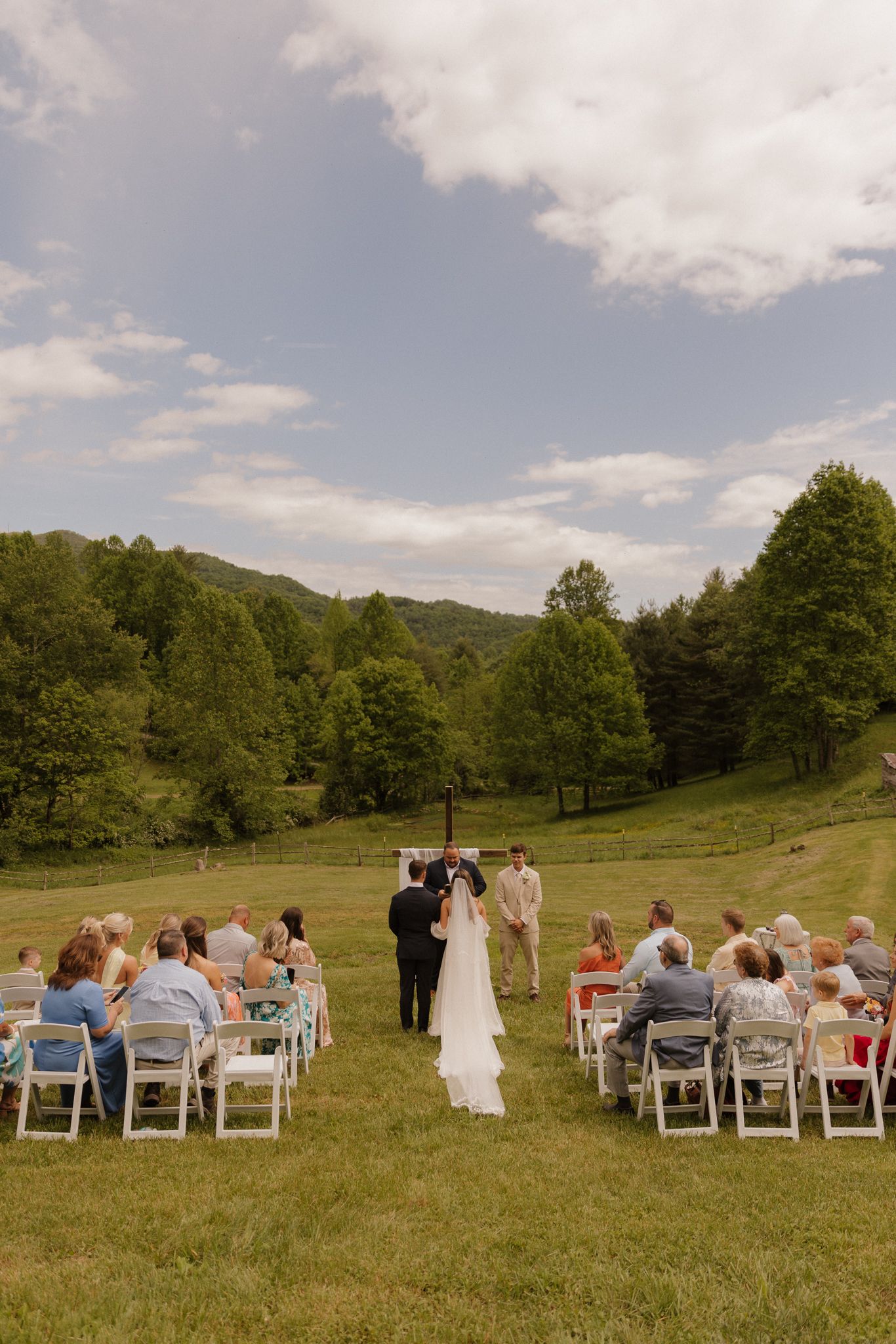 An outdoor wedding ceremony with white chairs set up on a grassy hillside.