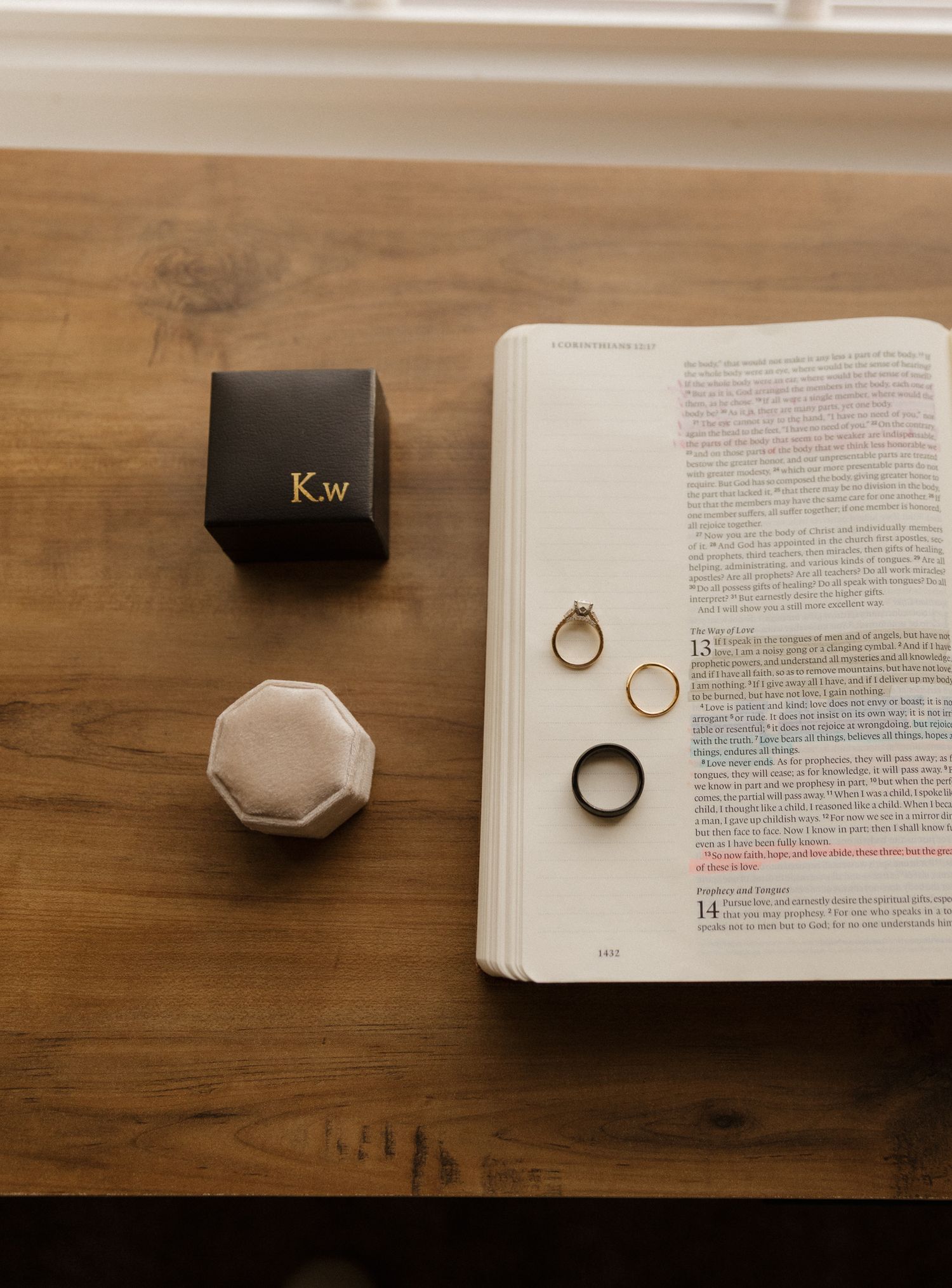 Wedding rings displayed on an open book next to jewelry boxes on wooden surface.