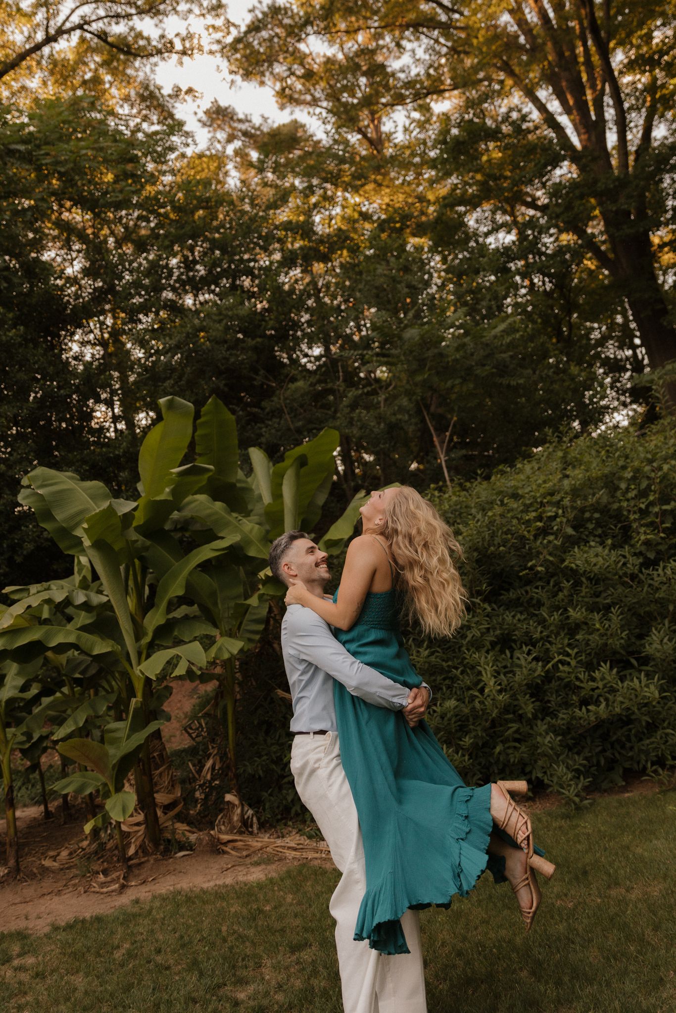 A romantic lift pose in a garden setting with a flowing teal dress at sunset.