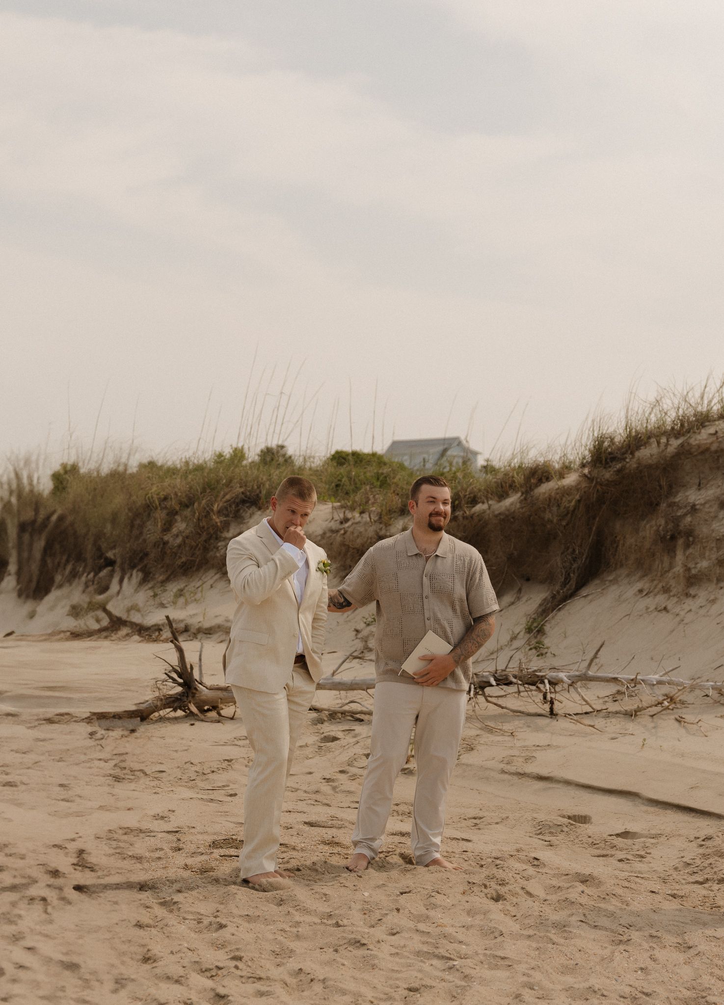 Groomsmen in light colored suits sharing a laugh on a beach.