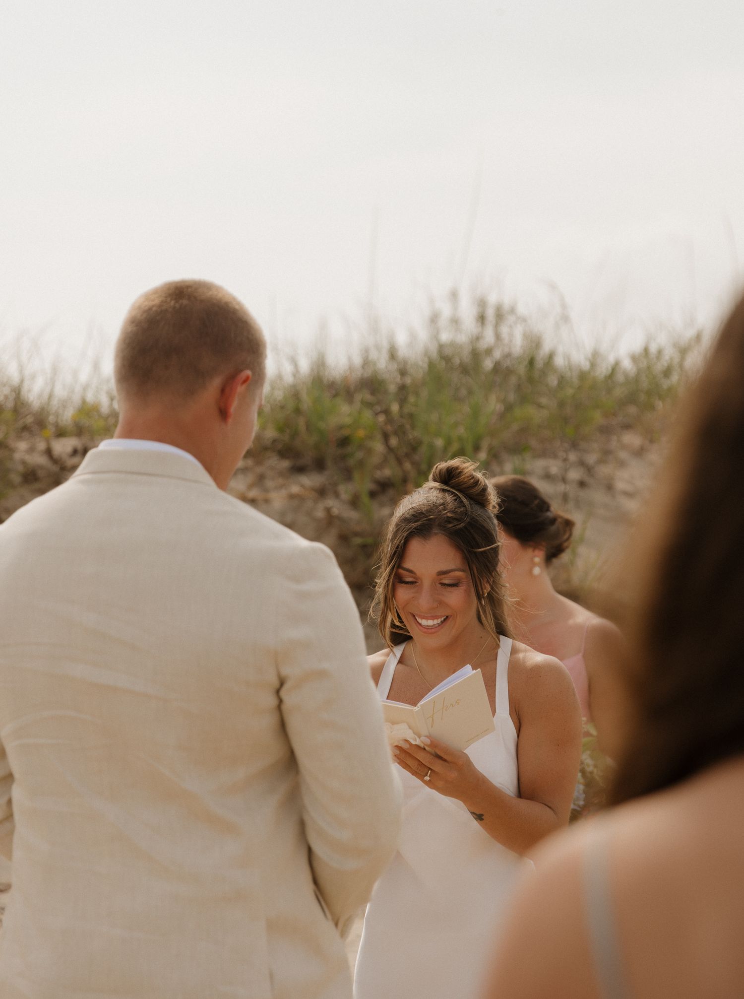Intimate beach wedding ceremony moment against coastal dunes.
