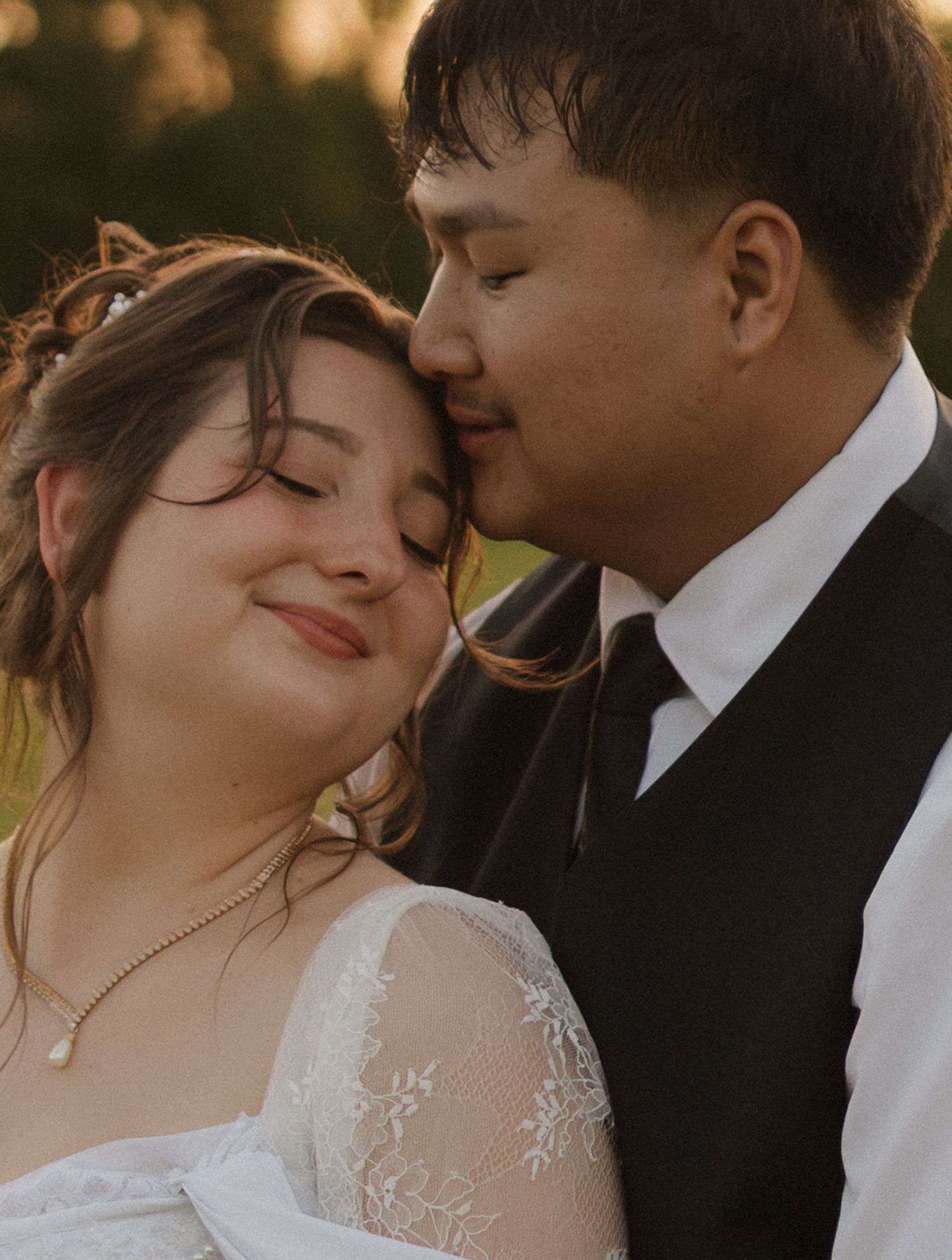 An intimate wedding portrait captures a romantic moment backlit by golden sunlight.