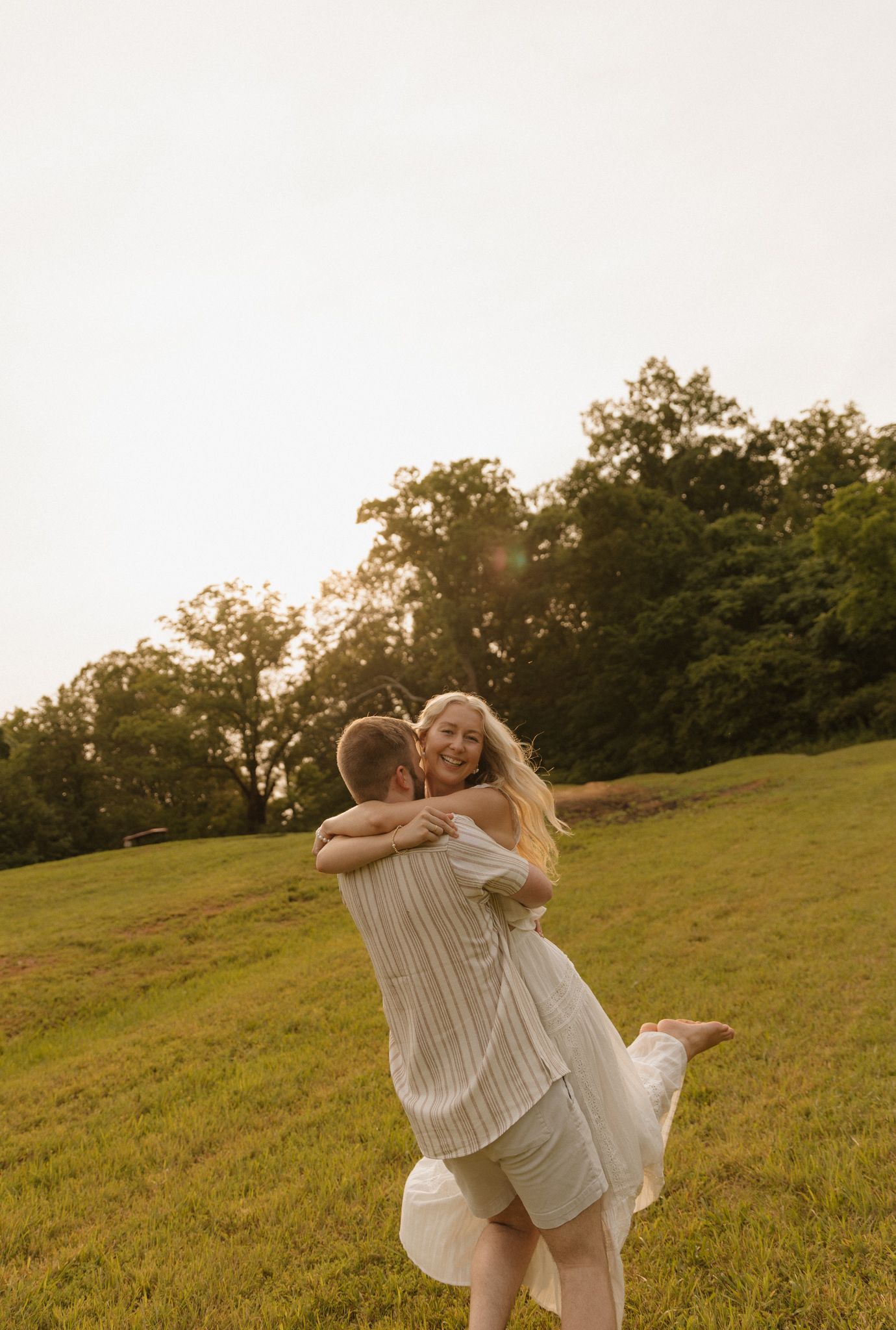 A joyful embrace on a grassy hillside during a warm summer evening.