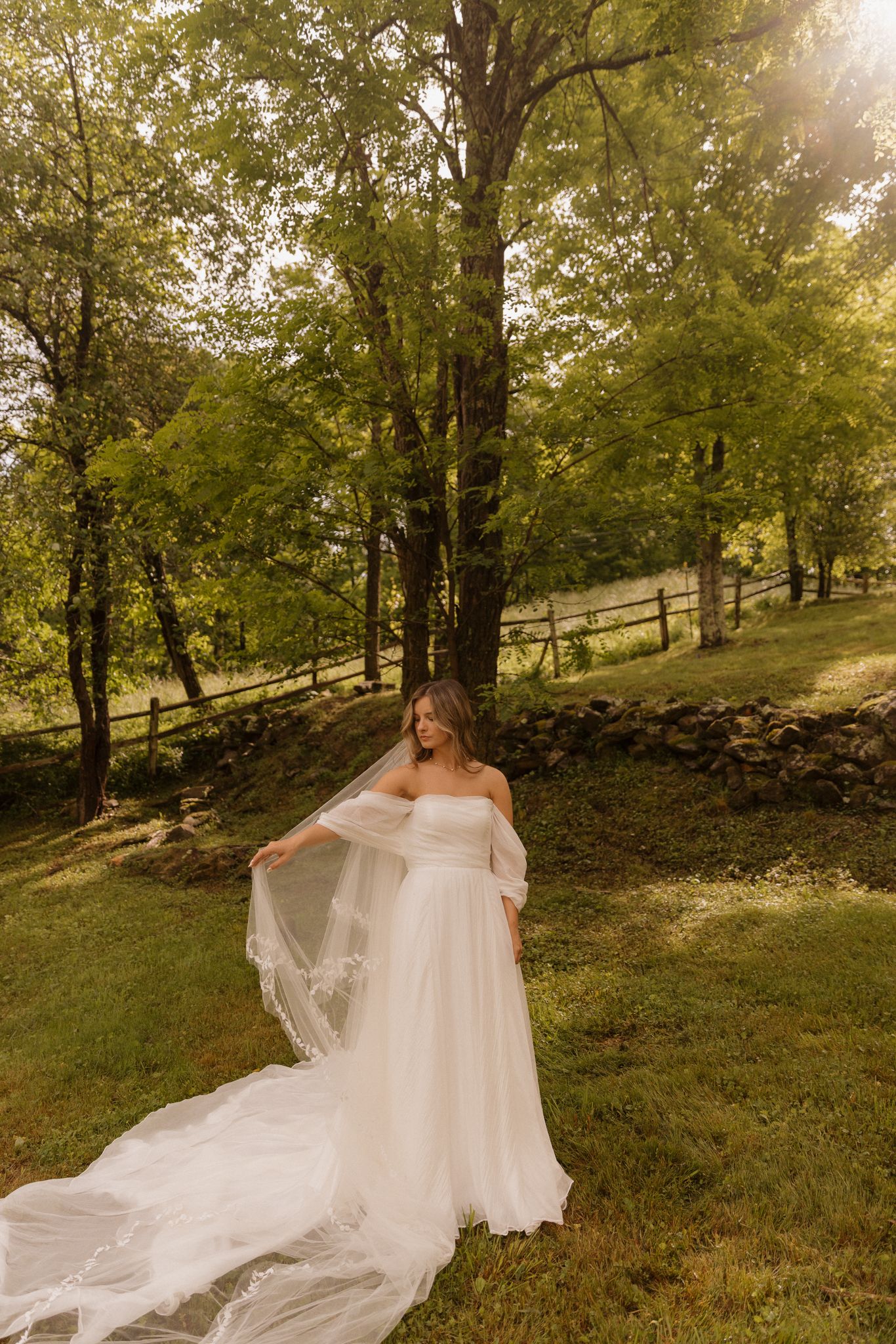 Flowing white wedding dress being showcased in golden sunlight among trees.
