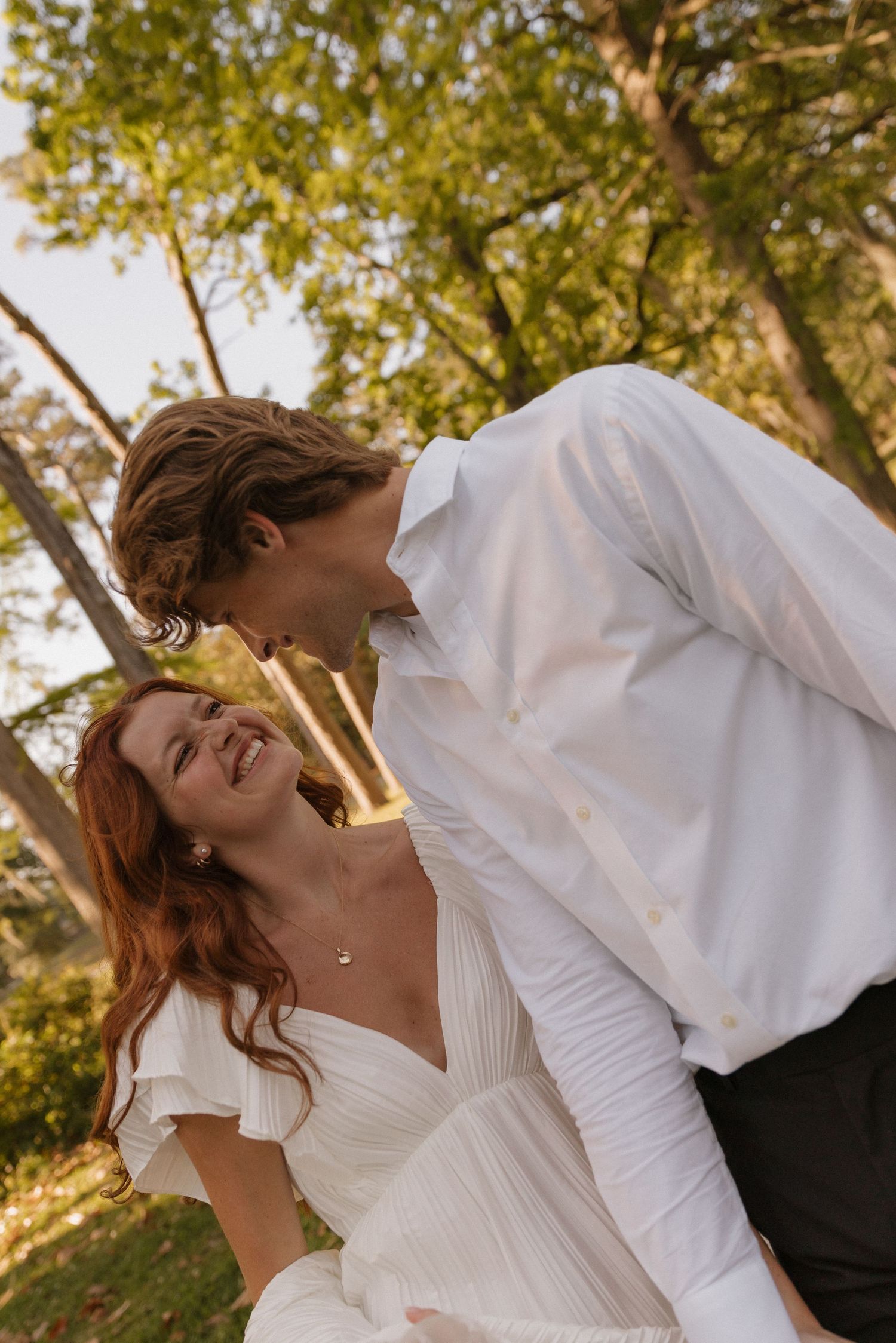 A romantic couple in white clothing embrace and share intimate moments in a sun-dappled outdoor setting.