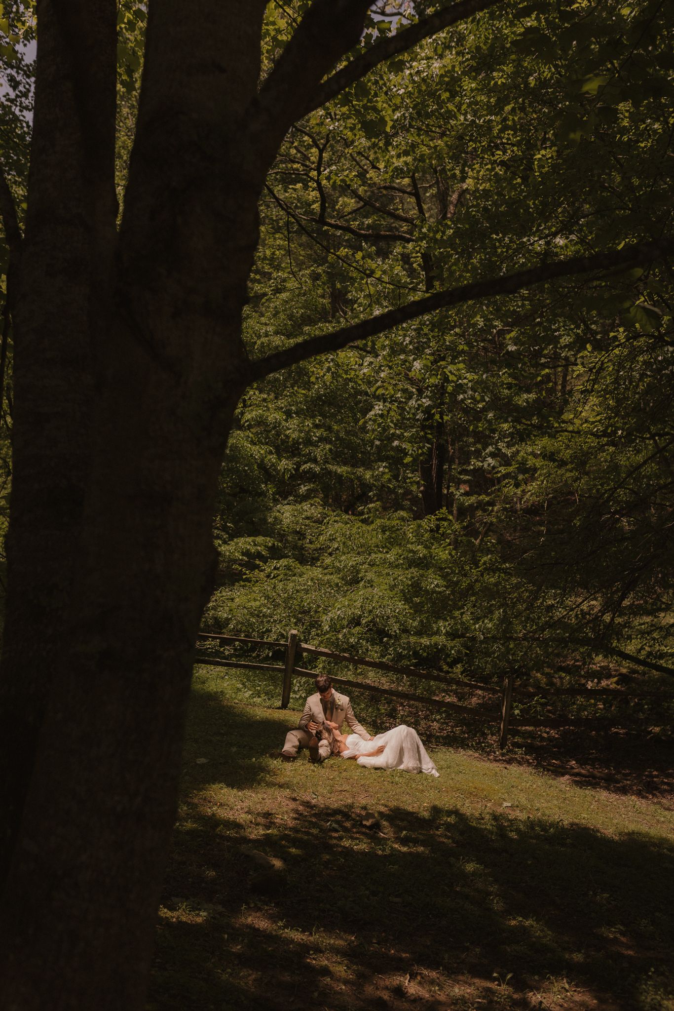 Couple rests together under a large tree in a wooded setting.
