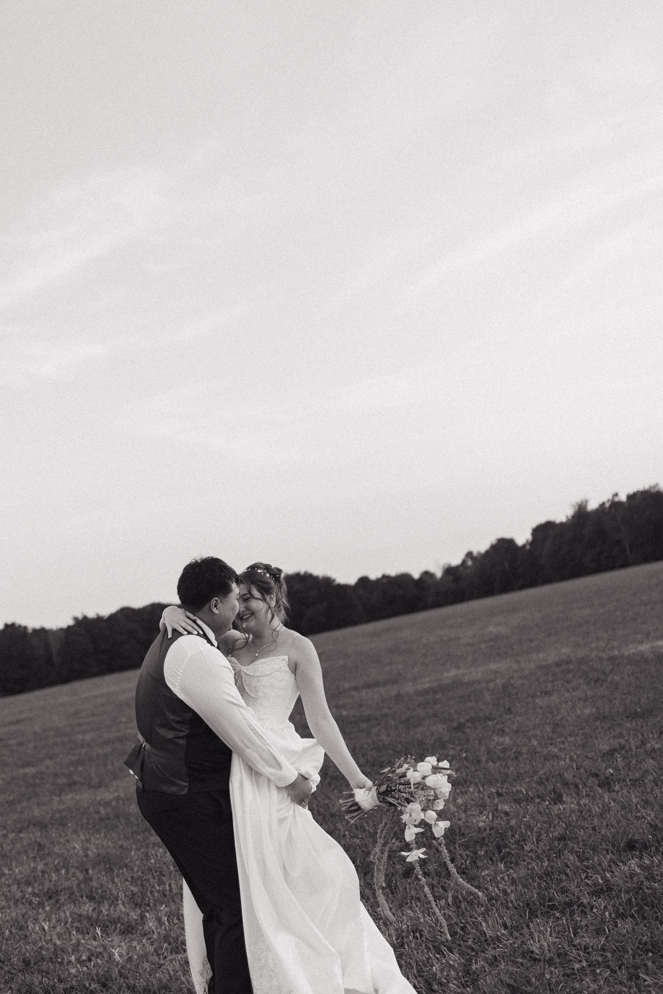 A black and white wedding portrait shows a tender embrace in an open field.