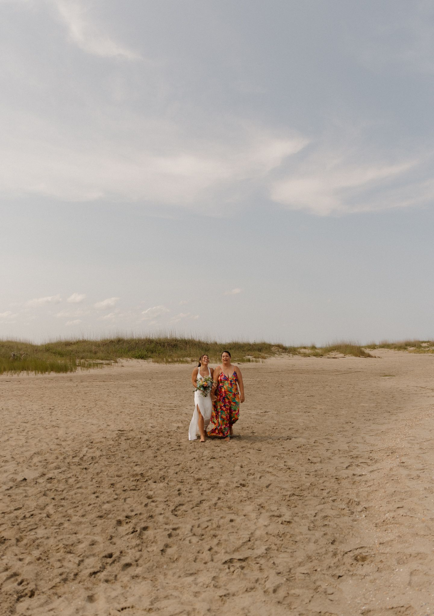 Wedding couple walking along a serene beach with sand dunes.