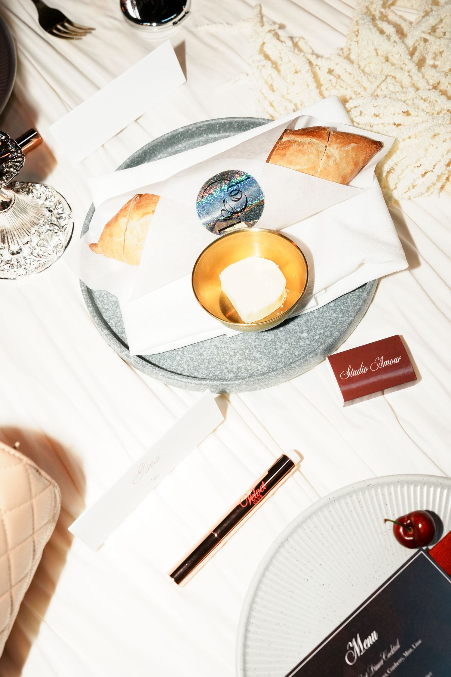 Elegant dining table setting with bread, butter dish, menu card, and gold pen on white linen.