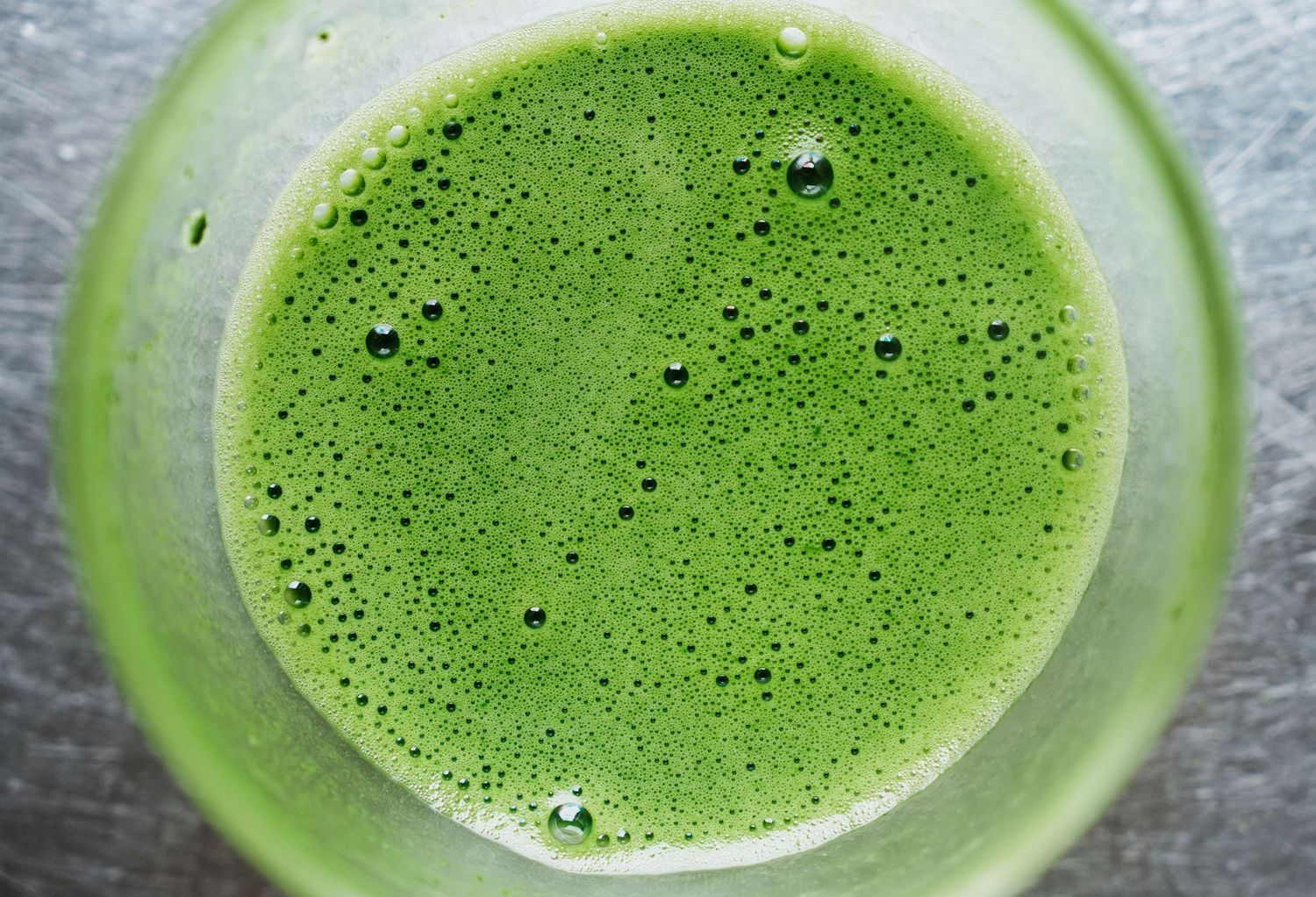 A frothy bright green matcha tea latte shown in multiple stages of preparation with bubbles forming on the surface.