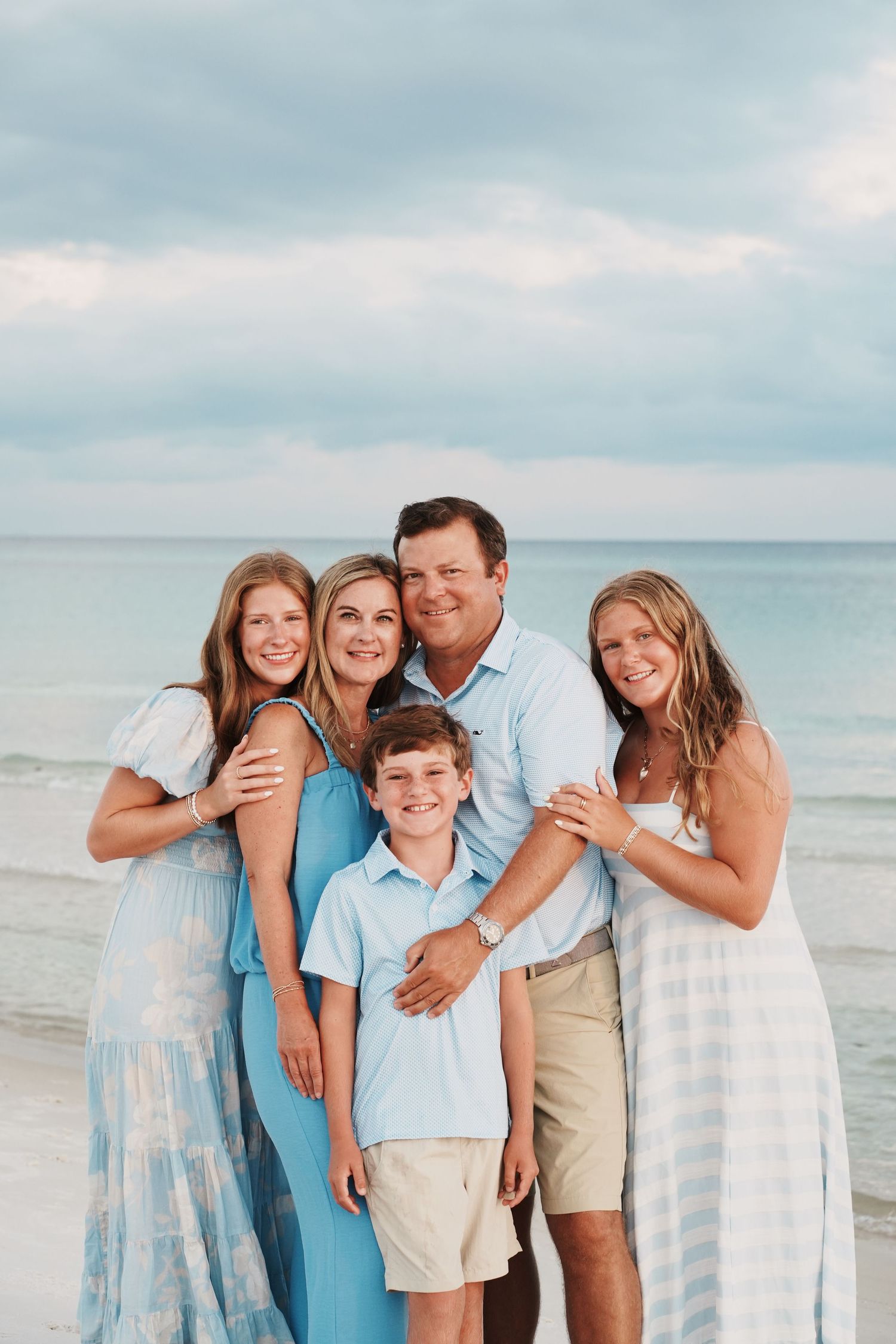 Candid beach family photos in soft blue and white clothing against serene ocean backdrop at sunset.