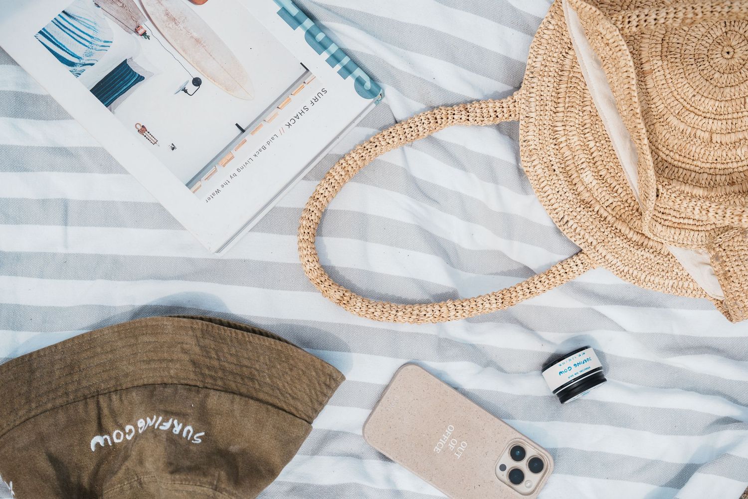 Flat lay of summer accessories with straw hat, sunglasses, phone, and white striped background.