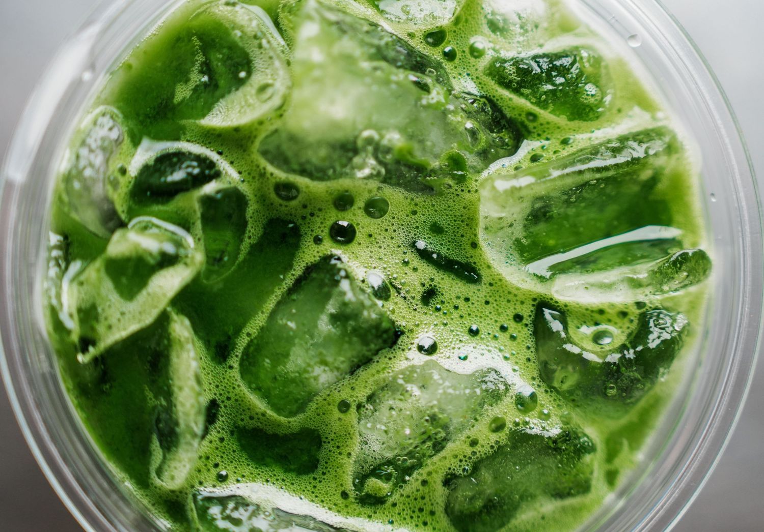 Close-up of vibrant green smoothies in clear glasses topped with fresh herbs and garnishes.