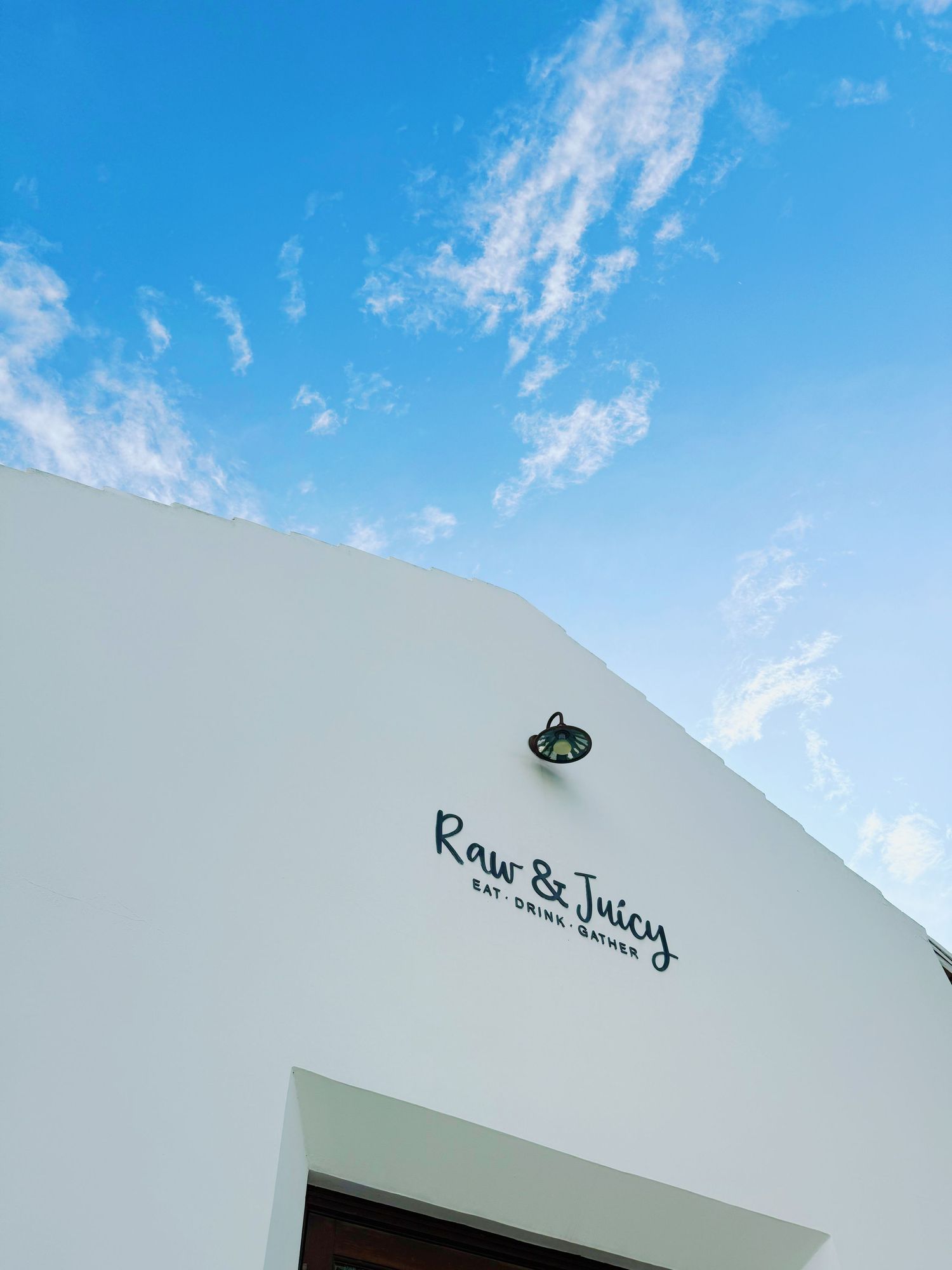 Row of white stucco buildings with flat roofs against a bright blue sky dotted with wispy clouds.