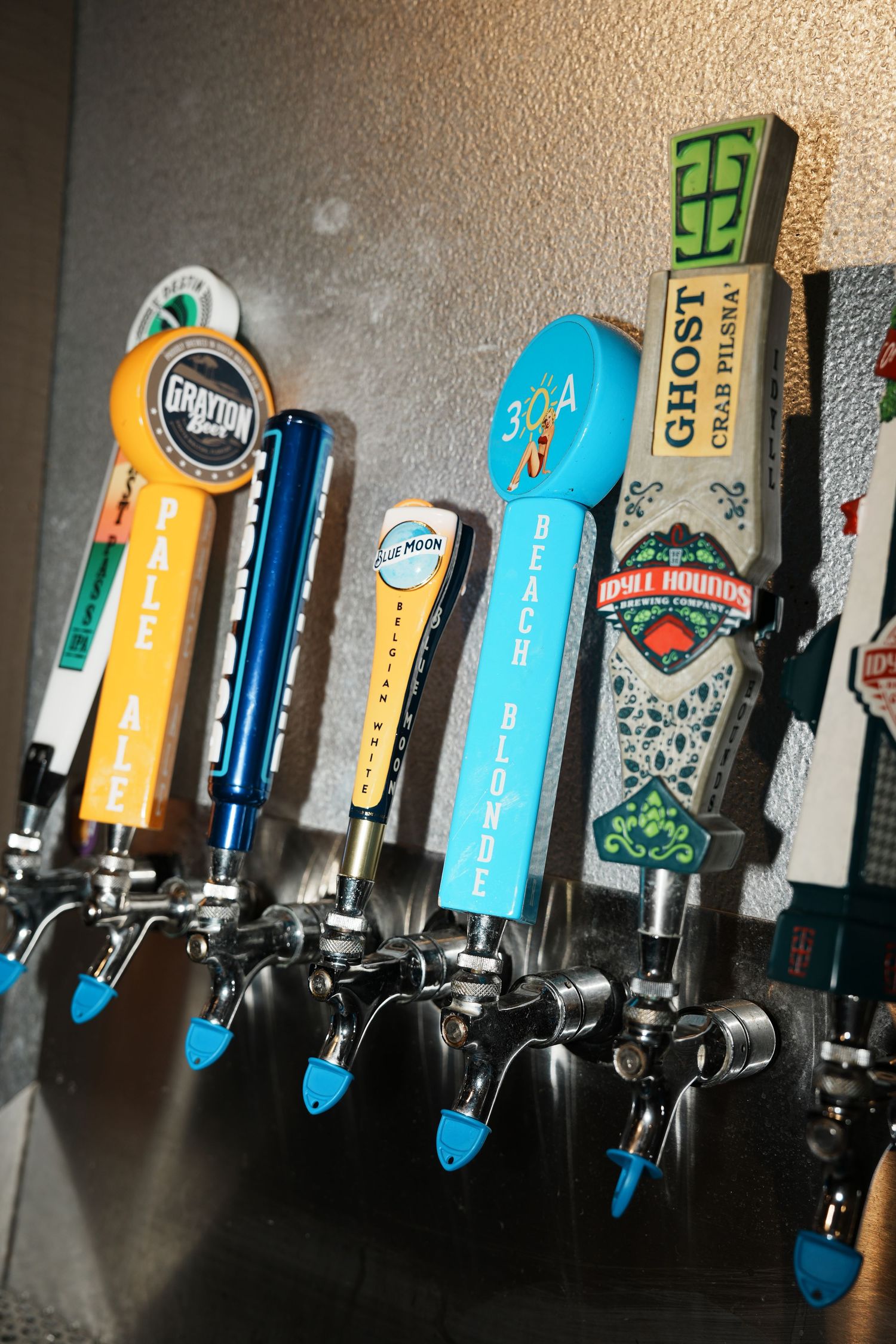 Row of colorful craft beer tap handles mounted on a bar wall showing various brewery logos and designs.