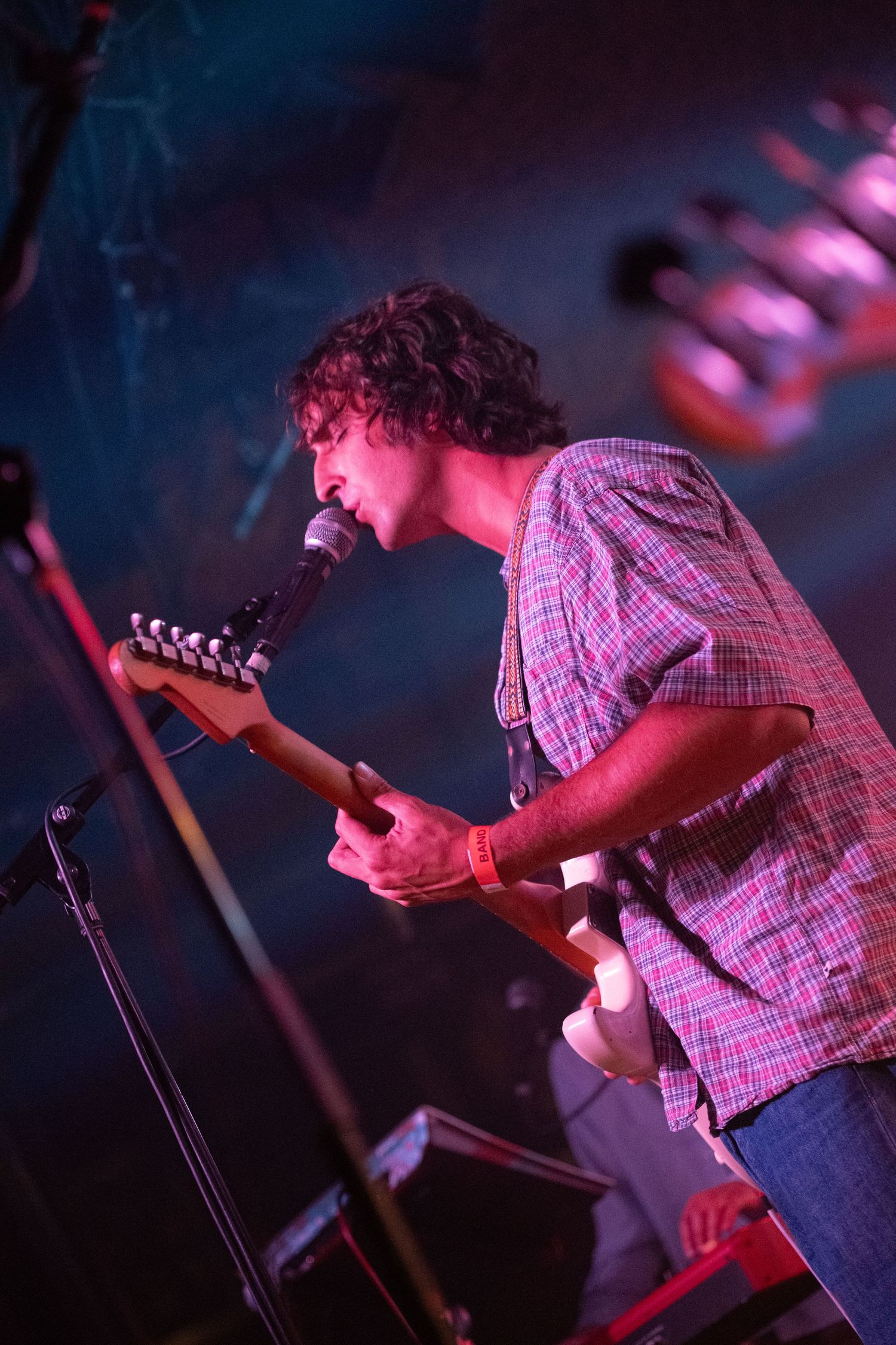 Musician performs on stage bathed in red and purple lighting while playing guitar and singing into microphone.
