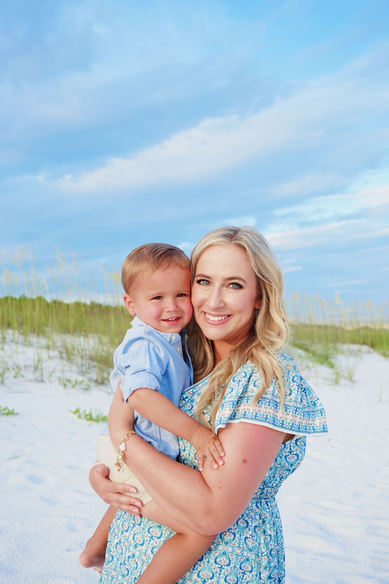 A parent and child share a joyful moment together on a sunny beach with white sand and blue skies.