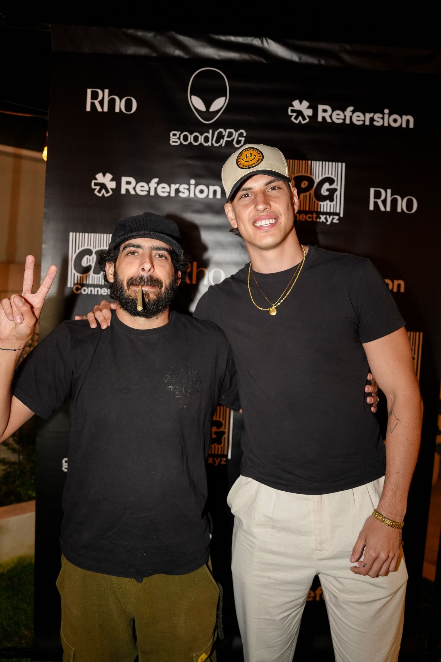 Two people in black shirts pose together at a promotional event with Rho and Refersion logos visible in background.