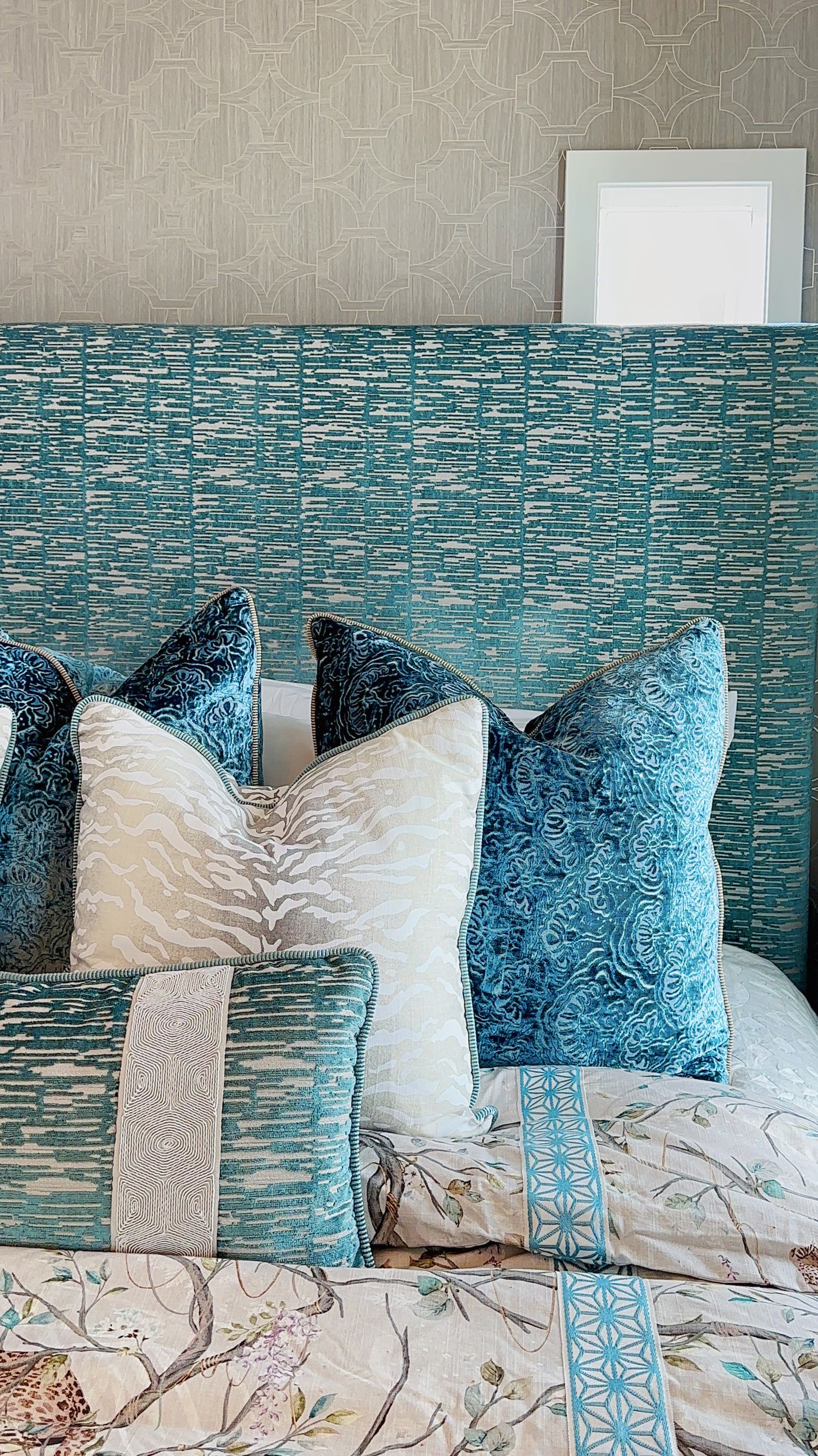 Luxurious bedroom decor featuring teal and white throw pillows against a textured wall with floral bedding and modern accents.