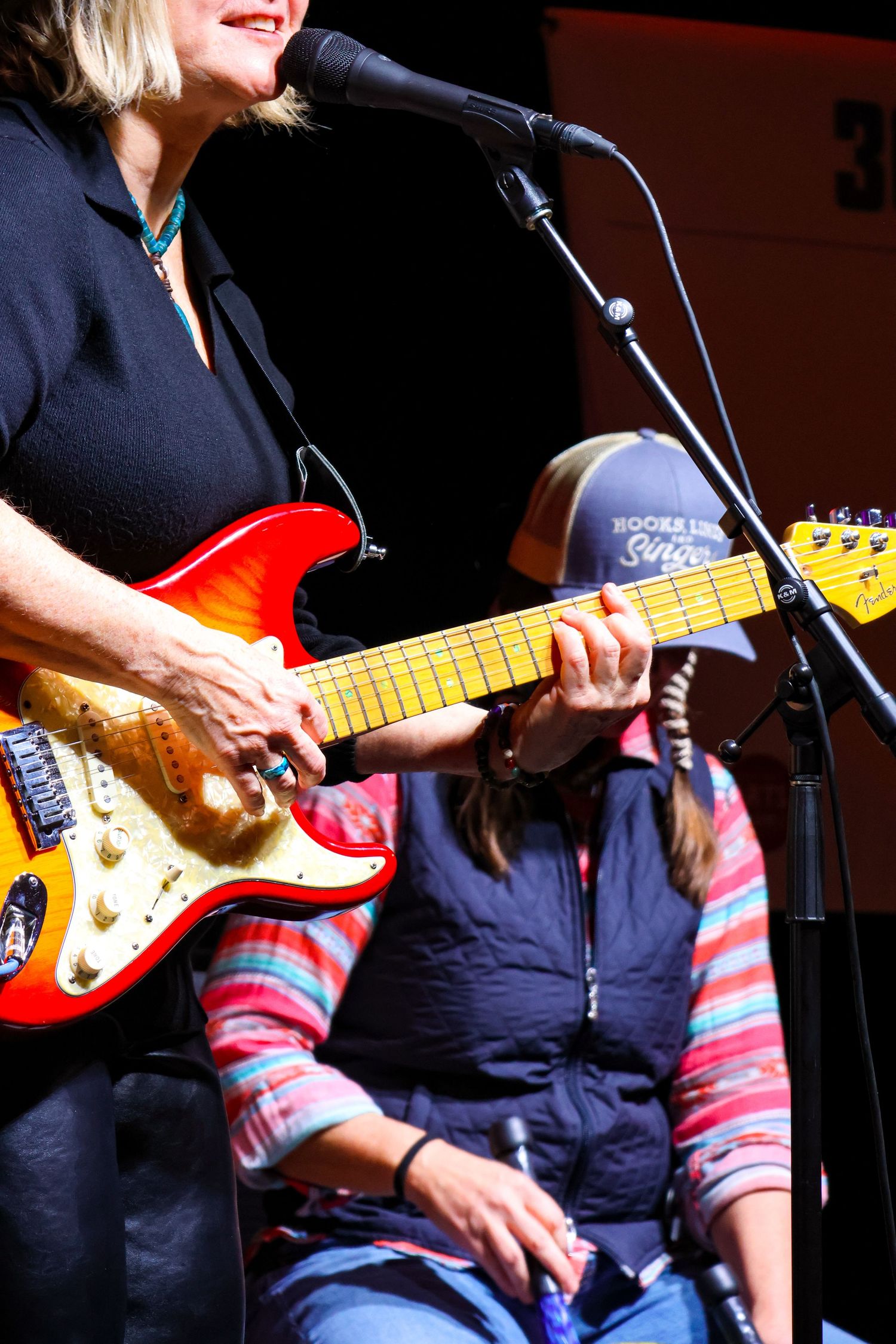 Performer playing red Stratocaster guitar on stage near microphone.