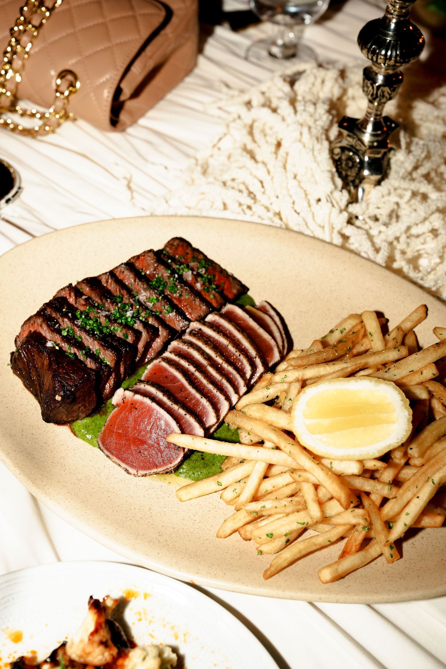 Sliced steak with chimichurri sauce and golden french fries served on an oval plate at an elegant restaurant.