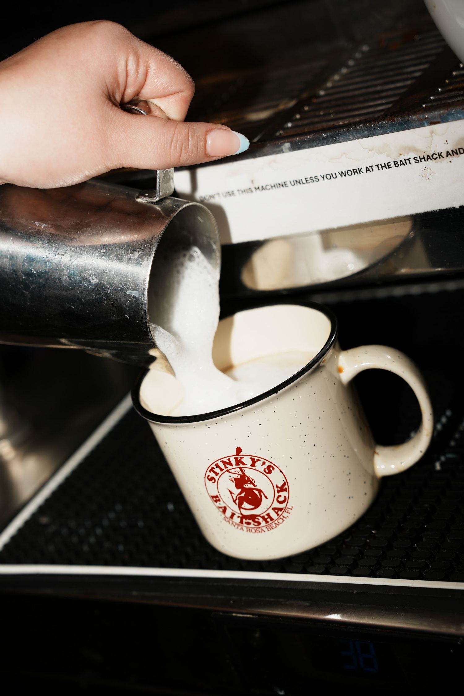 Multiple steps of pouring milk into a branded white coffee mug on a dark surface.
