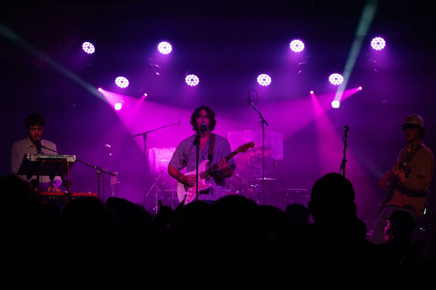 A silhouetted crowd enjoys a concert with purple stage lighting and fog creating an atmospheric ambiance.