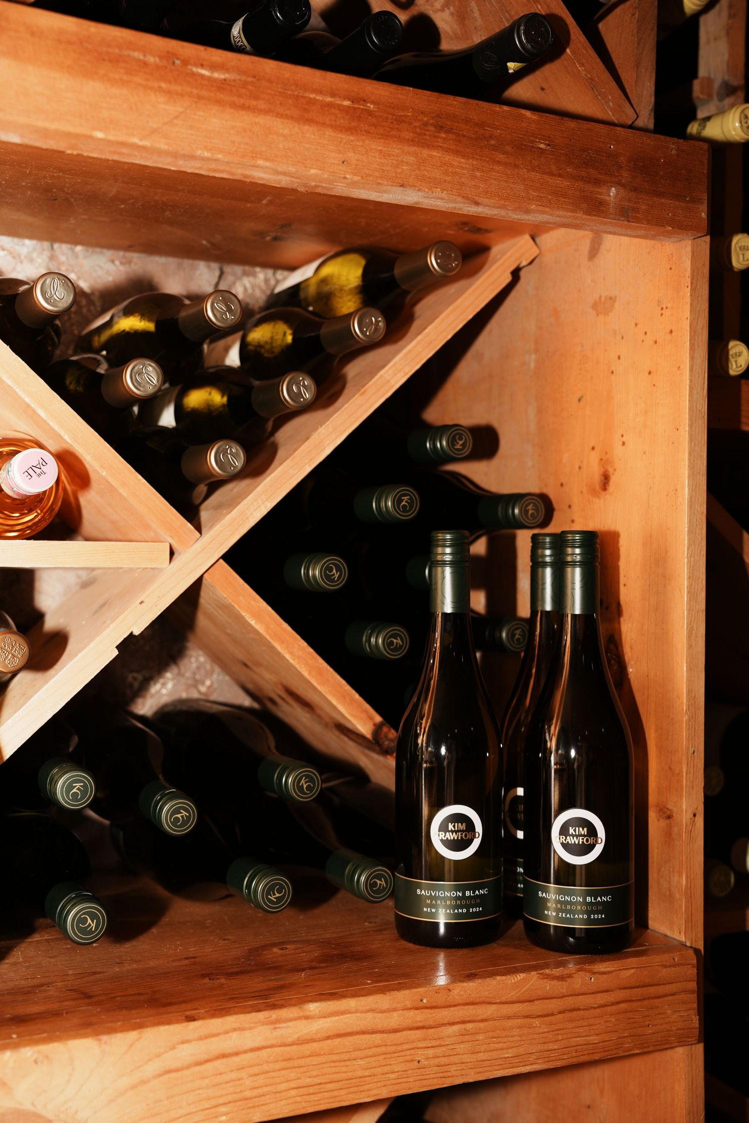 Wooden wine rack with diagonal cross supports displaying multiple dark wine bottles in organized storage compartments.