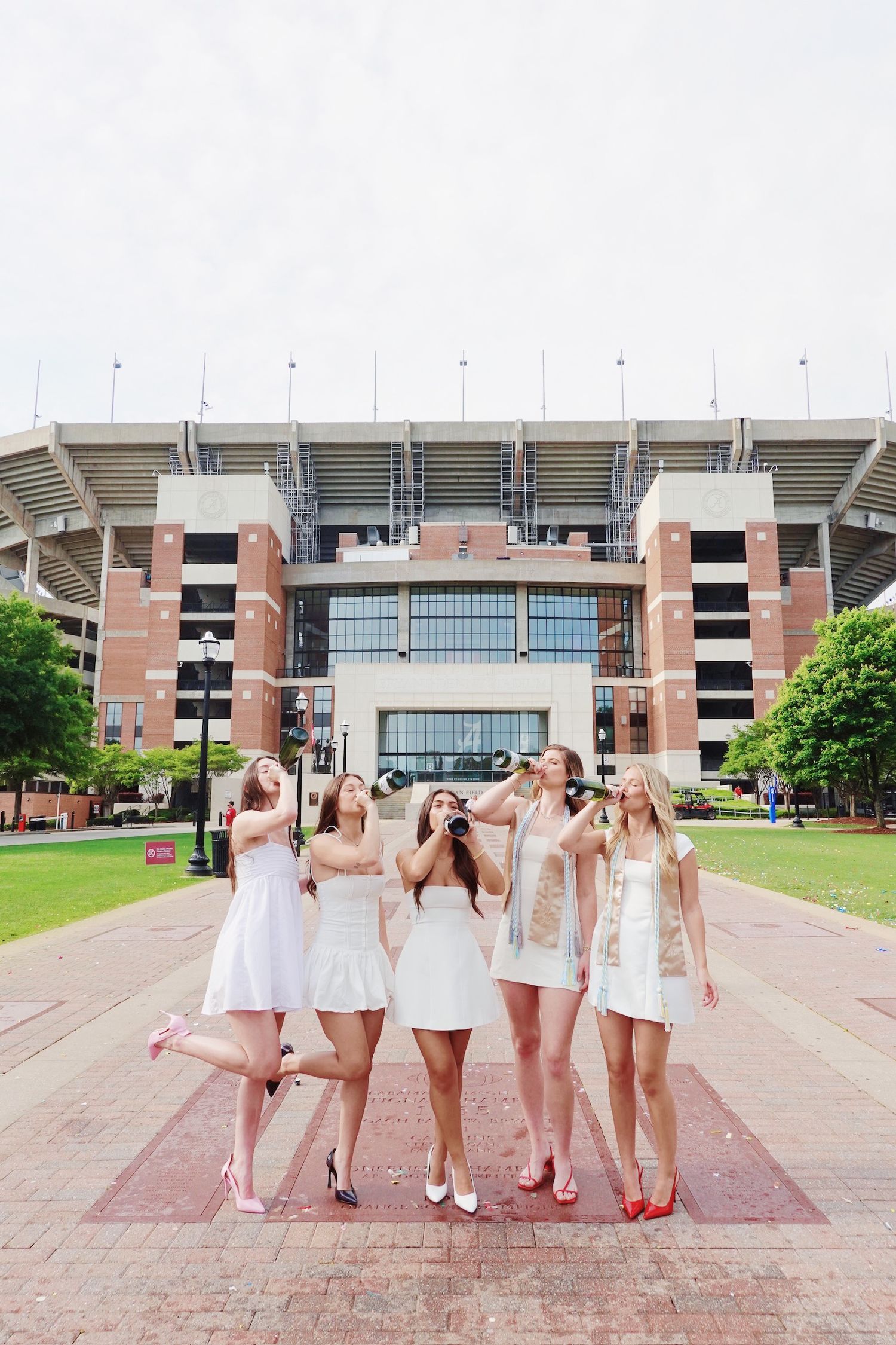 A group of friends in white dresses pose together in front of Bryant-Denny Stadium at the University of Alabama.