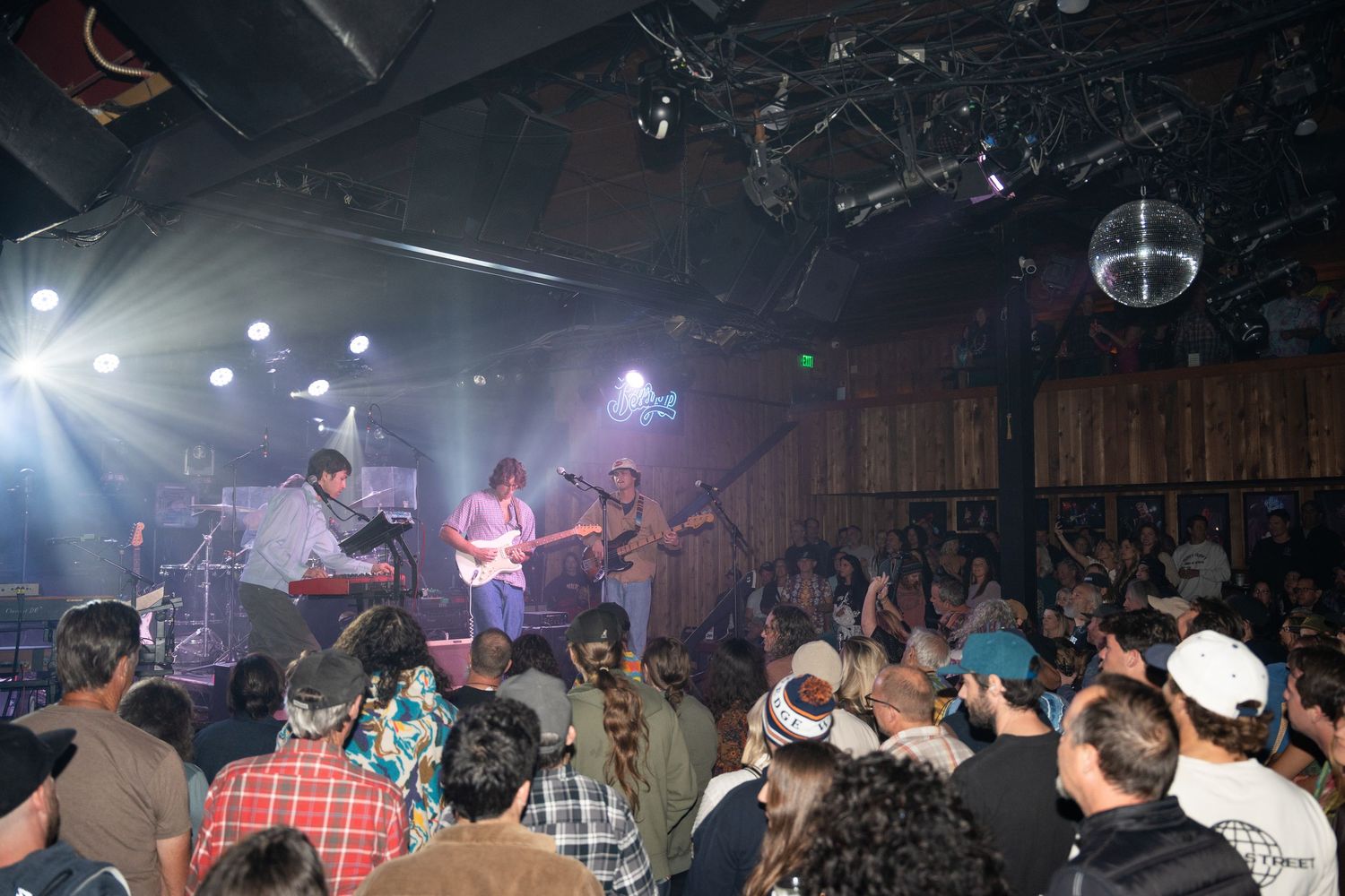A crowded nightclub dance floor filled with people enjoying live music under colorful stage lighting.
