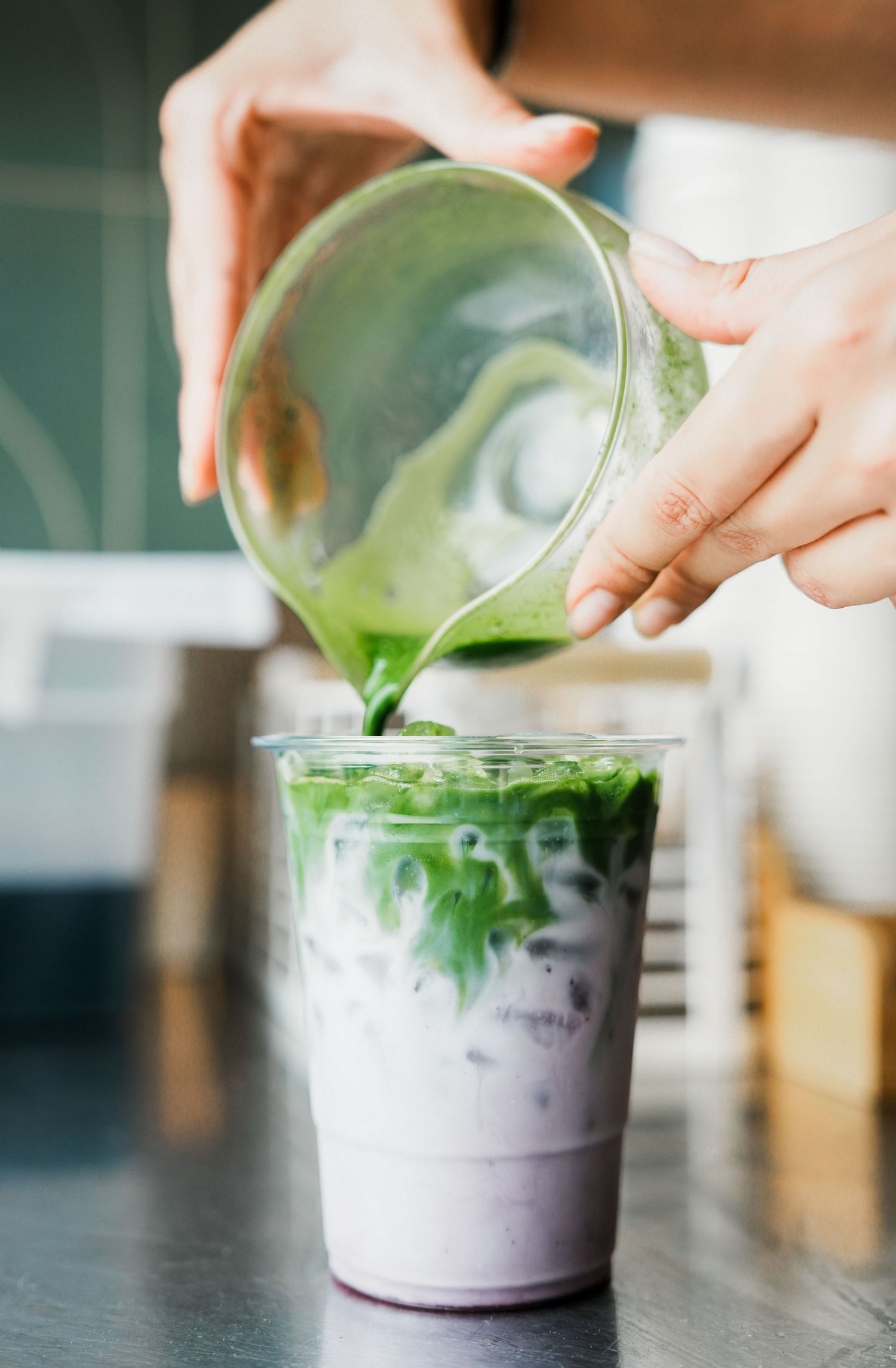 Green matcha being poured into an iced drink with white foam in a clear plastic cup.