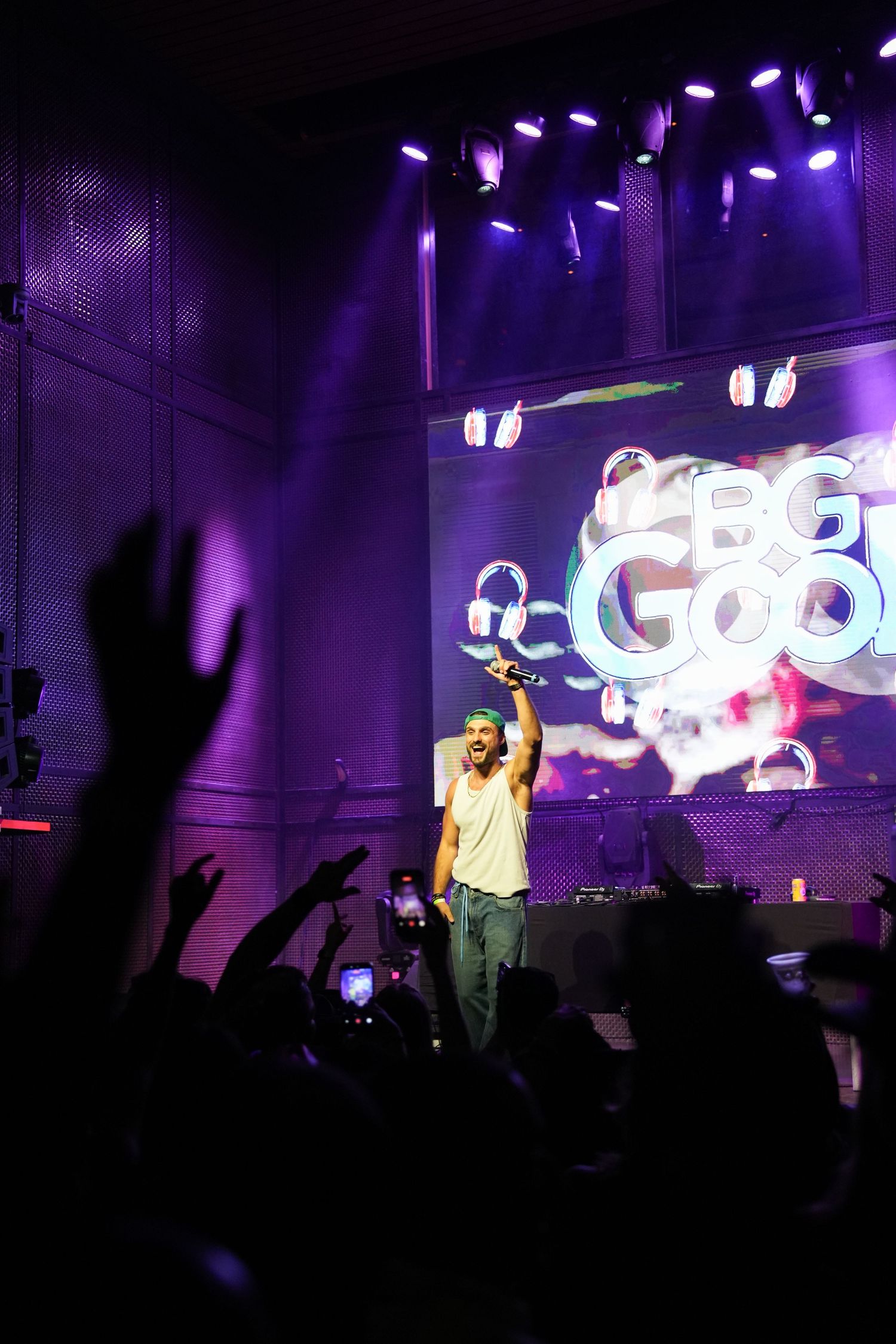 Concert performer on stage with purple lighting and silhouetted crowd raising hands during energetic live performance.