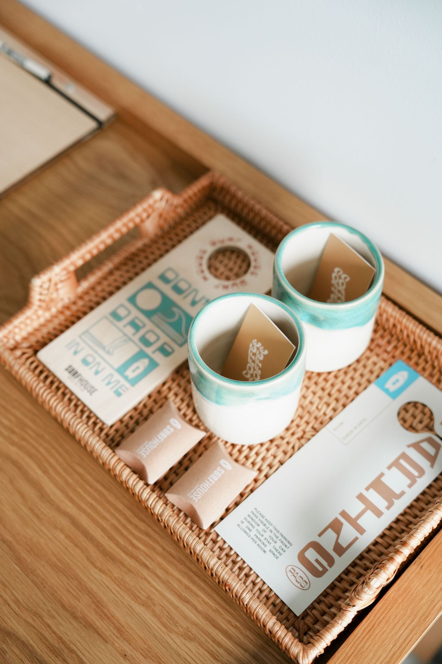 A woven wicker tray holds a white and turquoise ceramic tea set with modern minimalist packaging design.