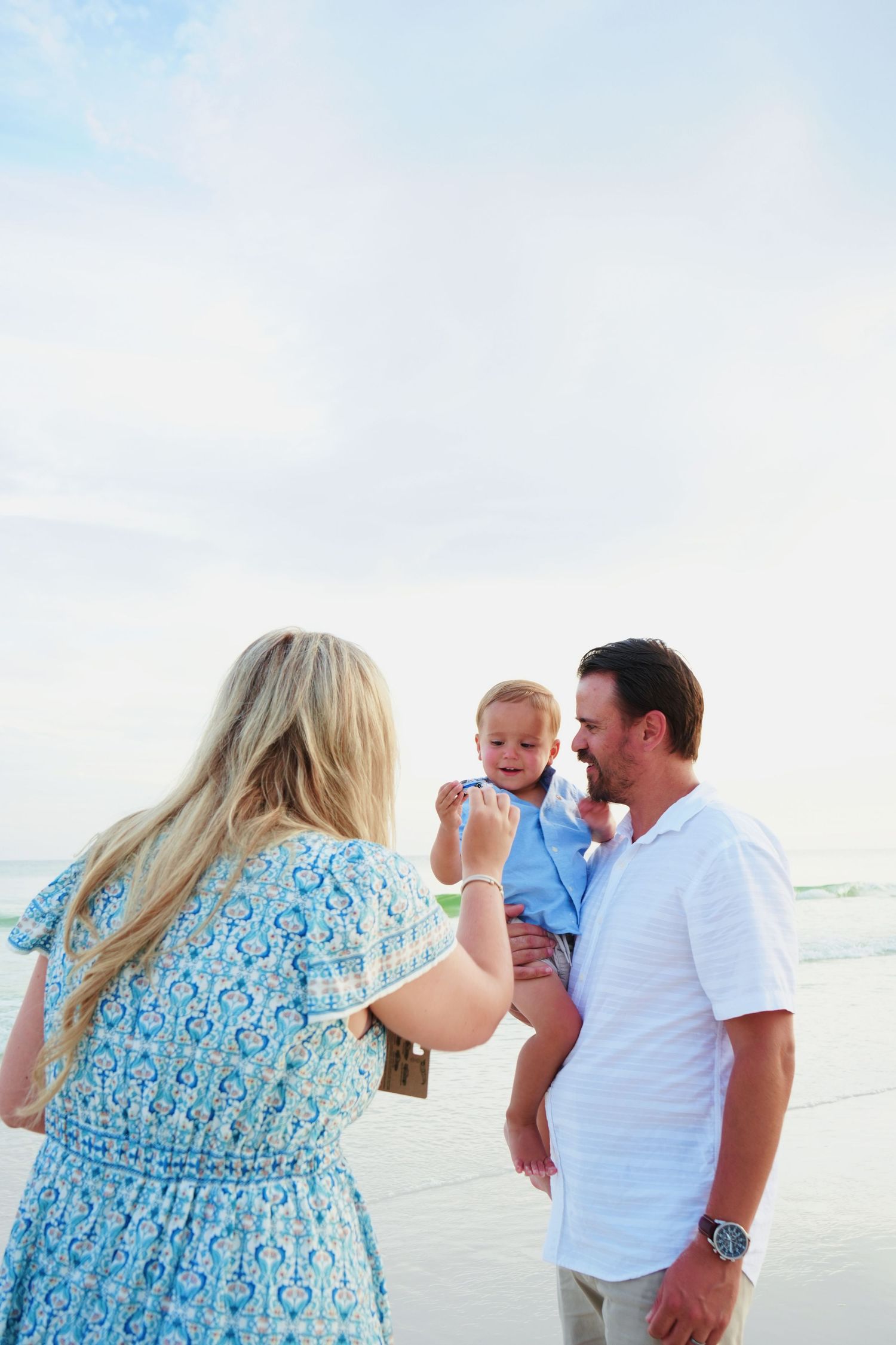 A joyful family moment captured on the beach with everyone dressed in light blue and white.