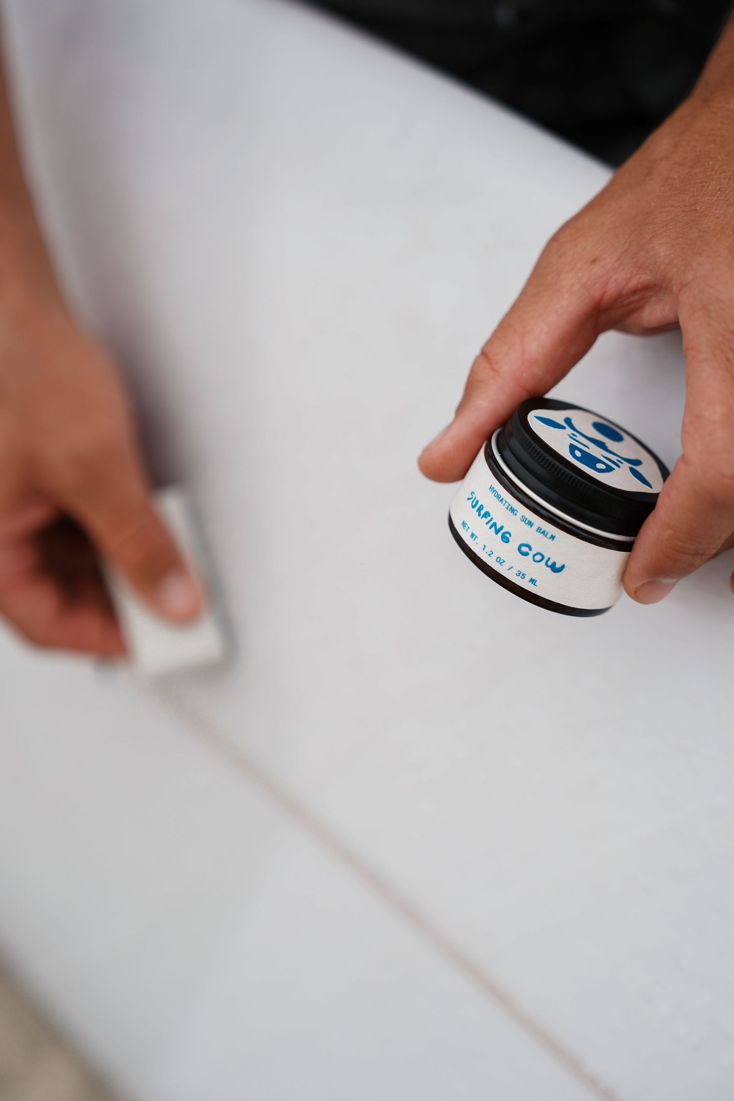 Hand reaching for a small blue and white skincare product jar on white surface.