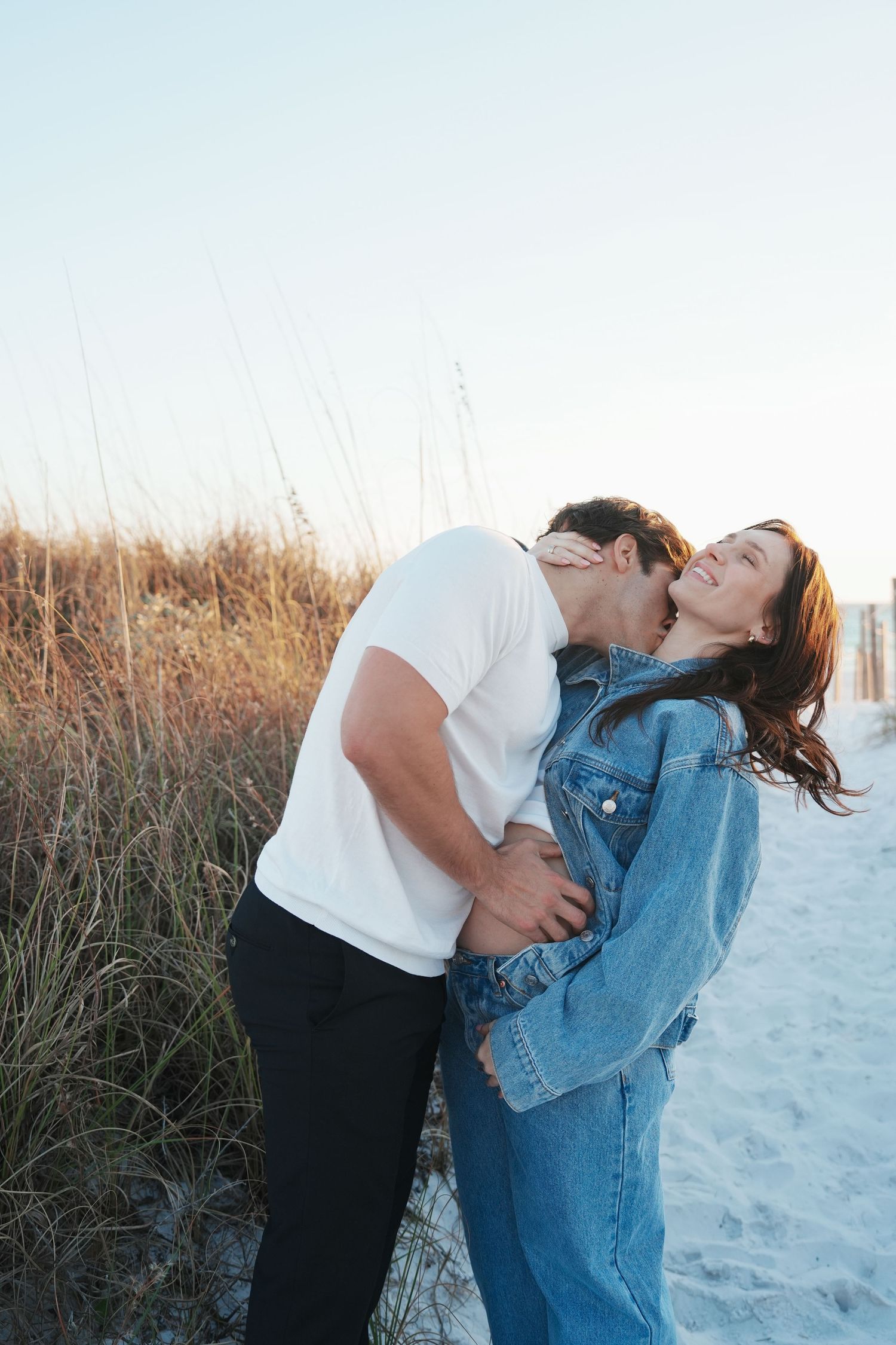 A romantic couple embracing and laughing together on a sandy beach at sunset.